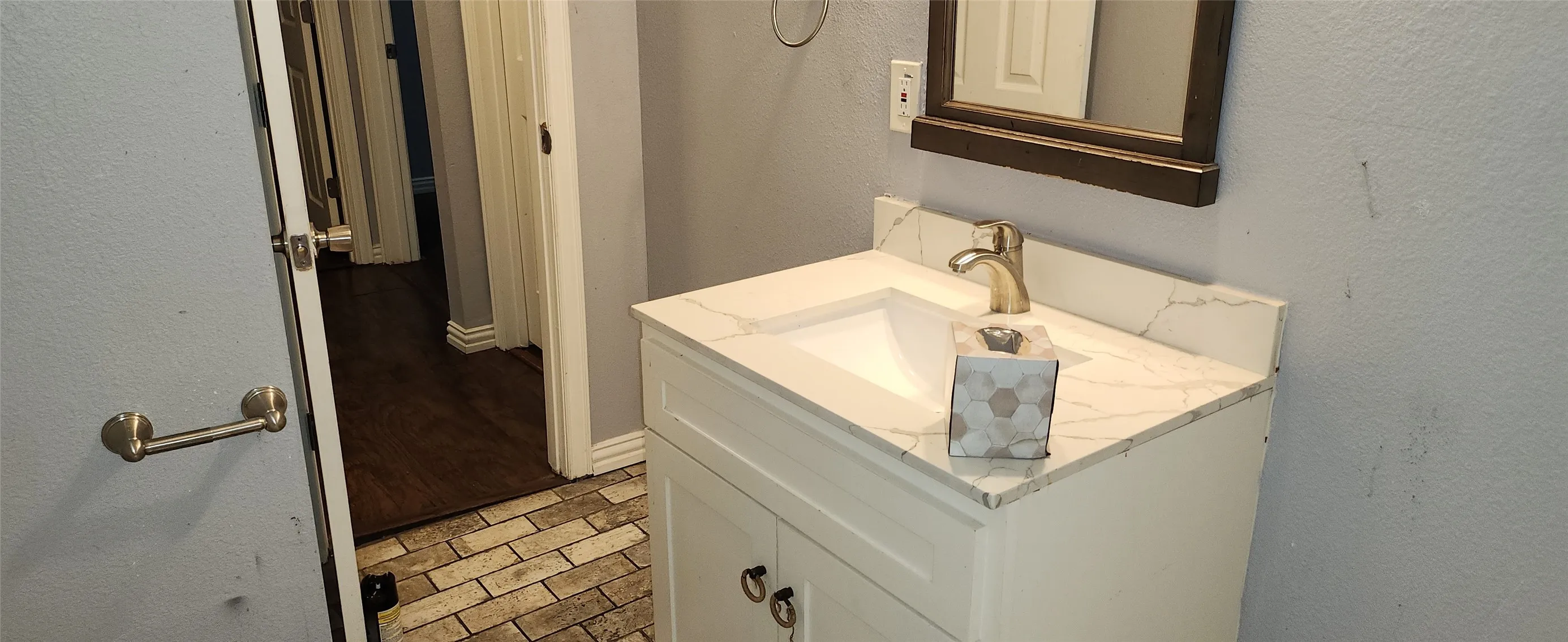White vanity with a rectangular sink, gold-tone faucet, and a stone-finish countertop
