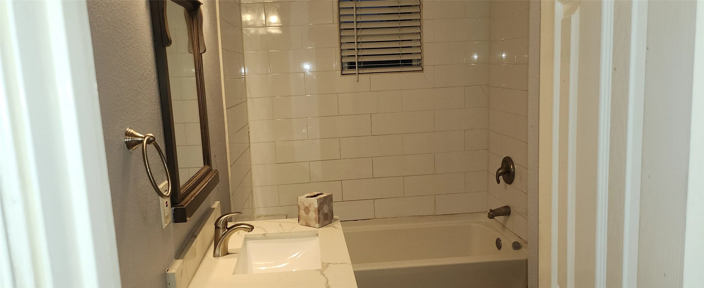 White subway tile shower surround, rectangular sink basin, brushed nickel faucet, and vanity with stone-look countertop