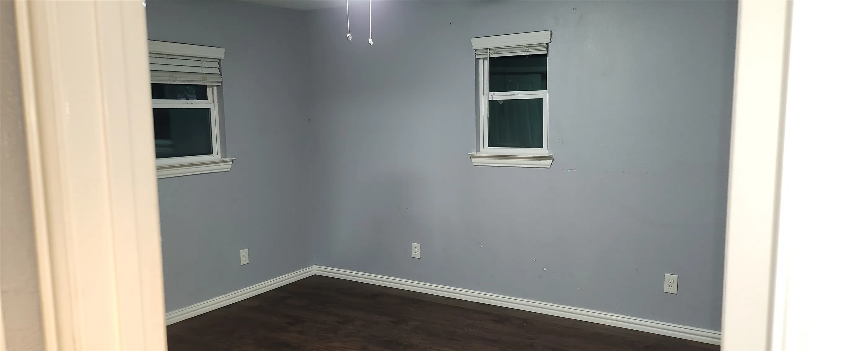 Light gray walls with wood-finish flooring and two windows with blinds