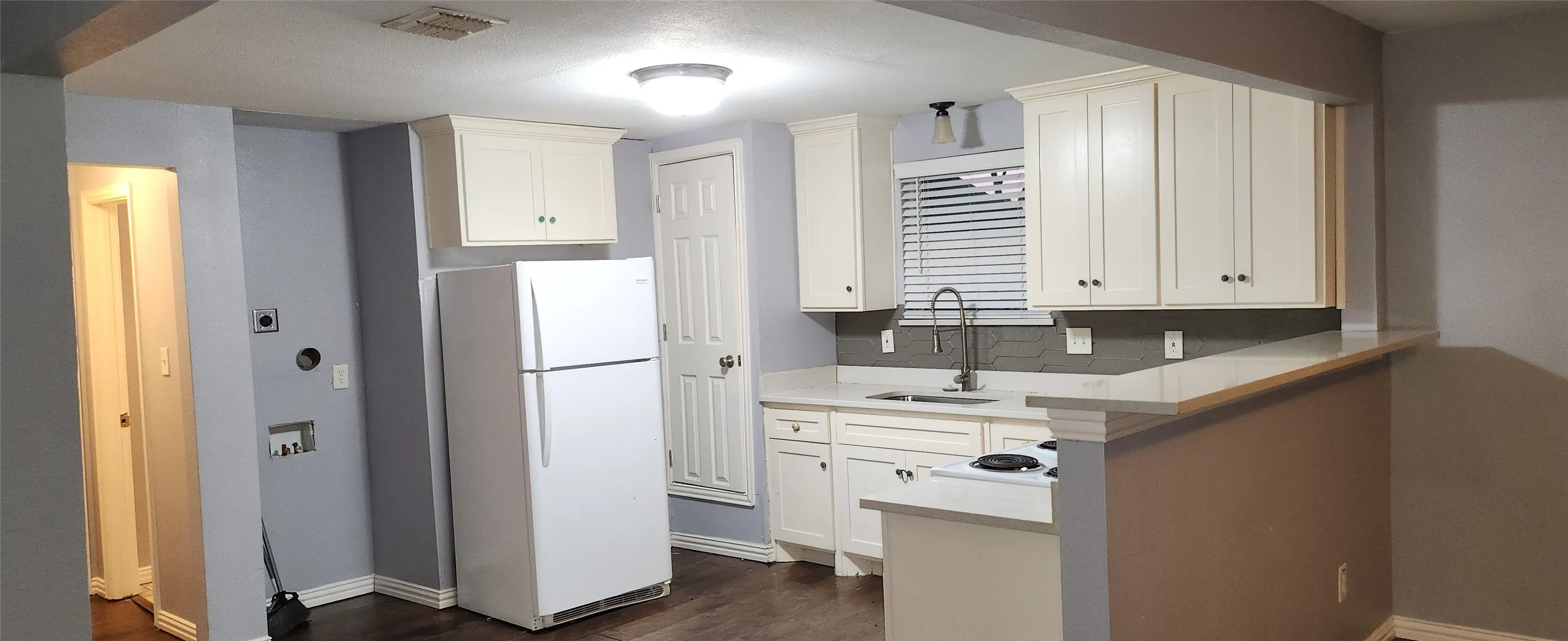 Kitchen featuring white cabinetry, light-toned countertops, a dark gray subway tile backsplash, and wood-finish flooring