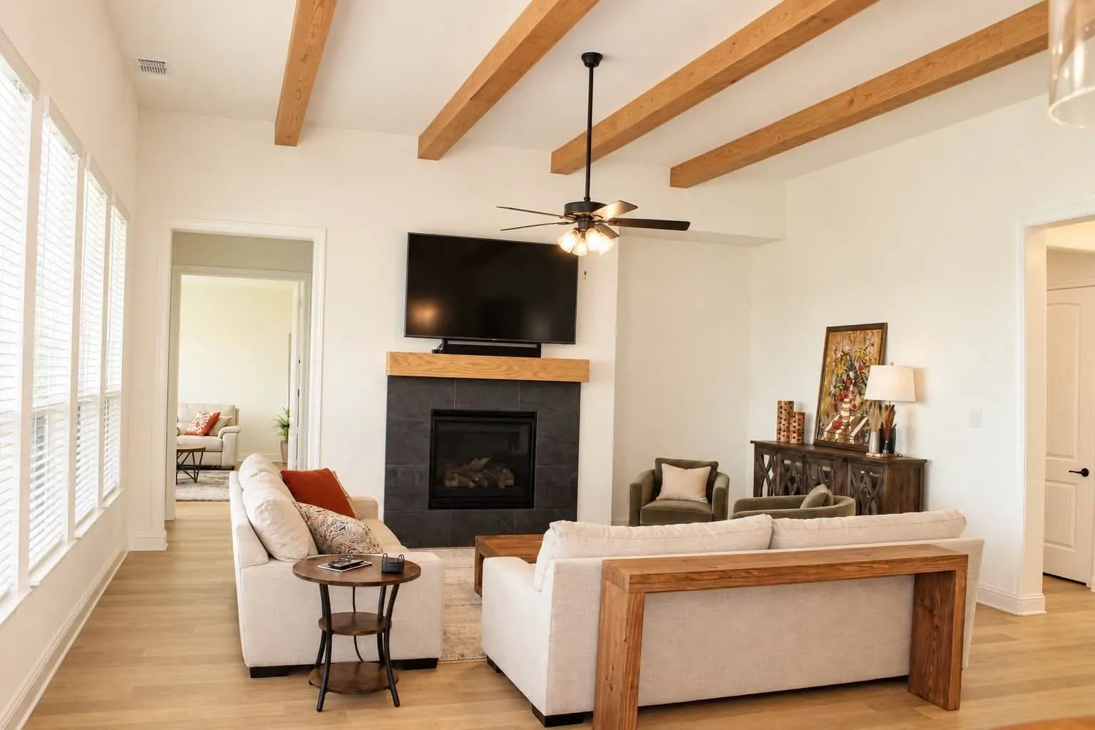 The living room showcases dramatic red oak beamed ceilings and a sliding patio door that opens to an extended covered patio and outdoor fireplace, creating the perfect indoor-outdoor entertaining space.