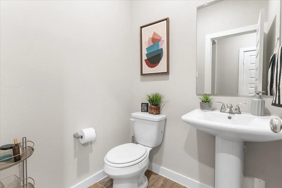 Pedestal sink with chrome fixtures, white toilet, and wood-finish flooring