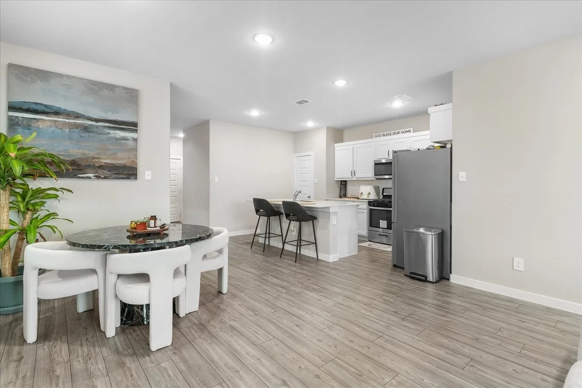 Wood-finish flooring throughout, recessed lighting, and a kitchen featuring white cabinetry, a kitchen island with seating, and stainless steel appliances