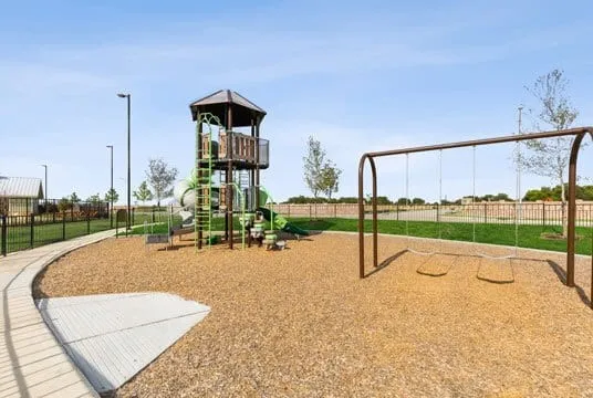 Community playground with a multi-level play structure, swing set, and wood chip surfacing