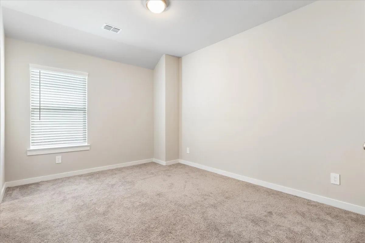 Neutral tone wall paint, textured carpeting, window with blinds, and flush-mount ceiling light