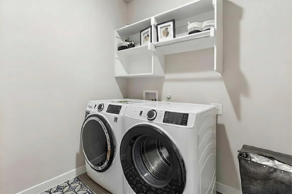 Integrated laundry area featuring mounted shelving, a built-in hanging rod, and light-toned walls