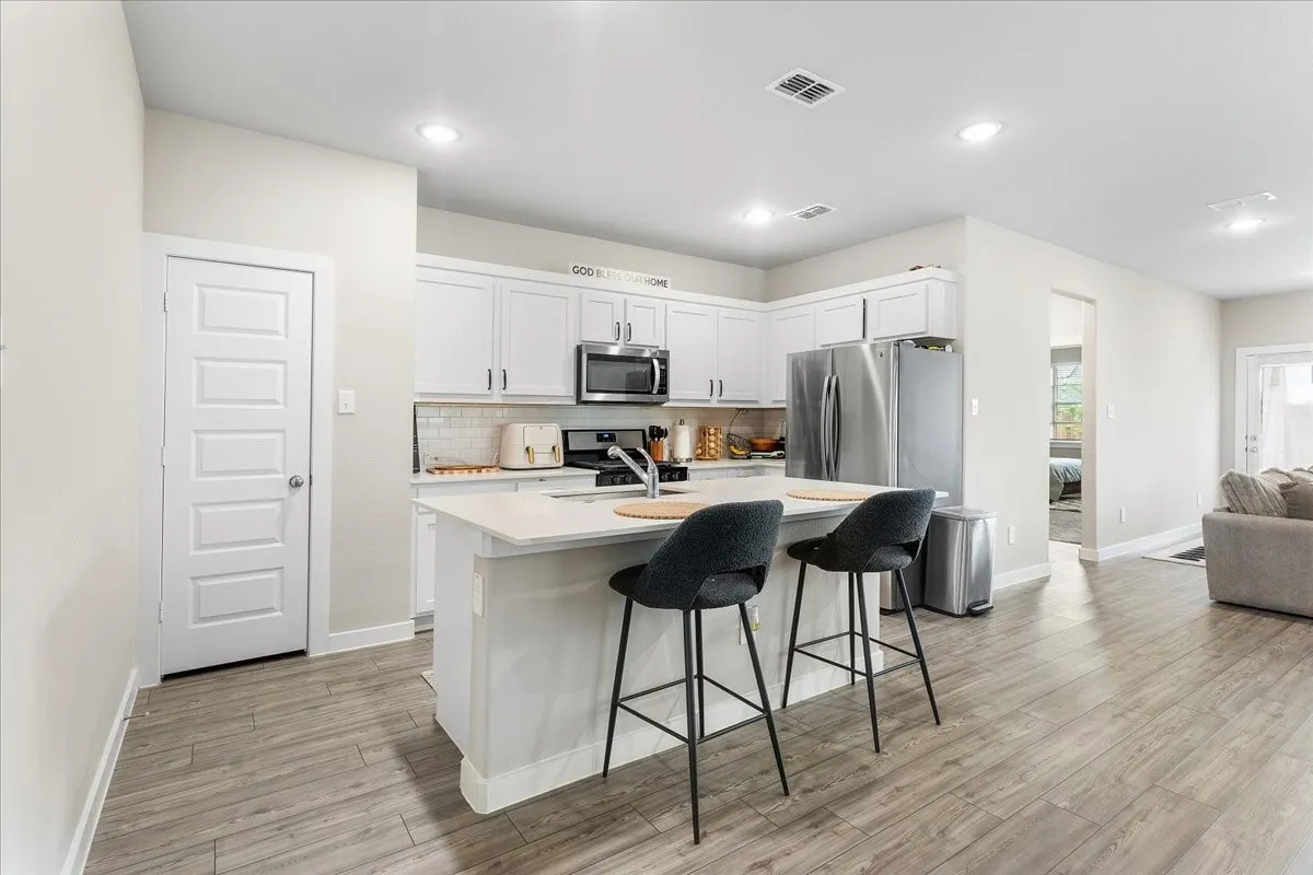 Kitchen featuring white cabinetry, stainless steel appliances, a center island with counter seating, and wood-finish flooring