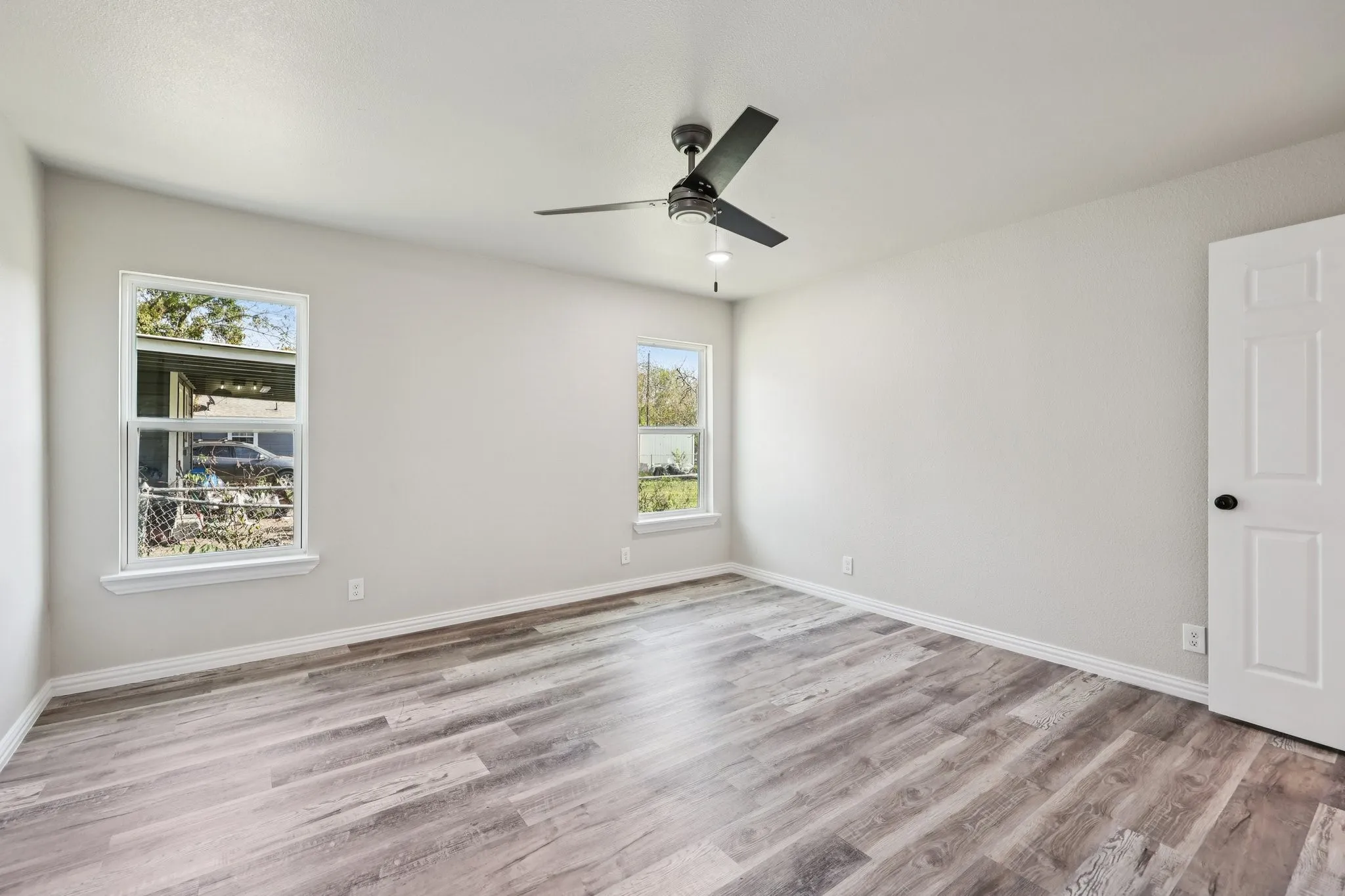 Neutral-toned room featuring two windows with white trim, wood-finish flooring, a contemporary ceiling fan, and a white panel door