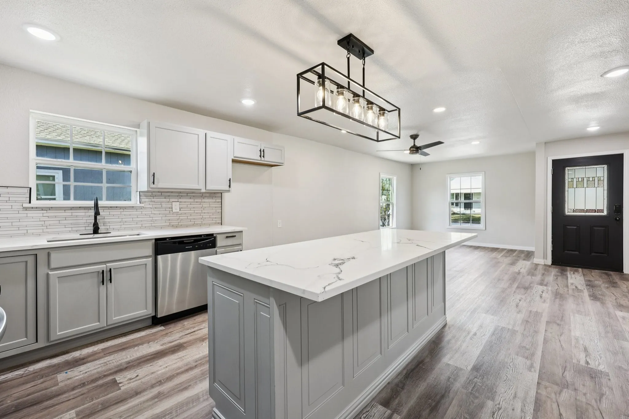 Open-concept kitchen featuring an expansive island with a stone-finish countertop and paneling detail