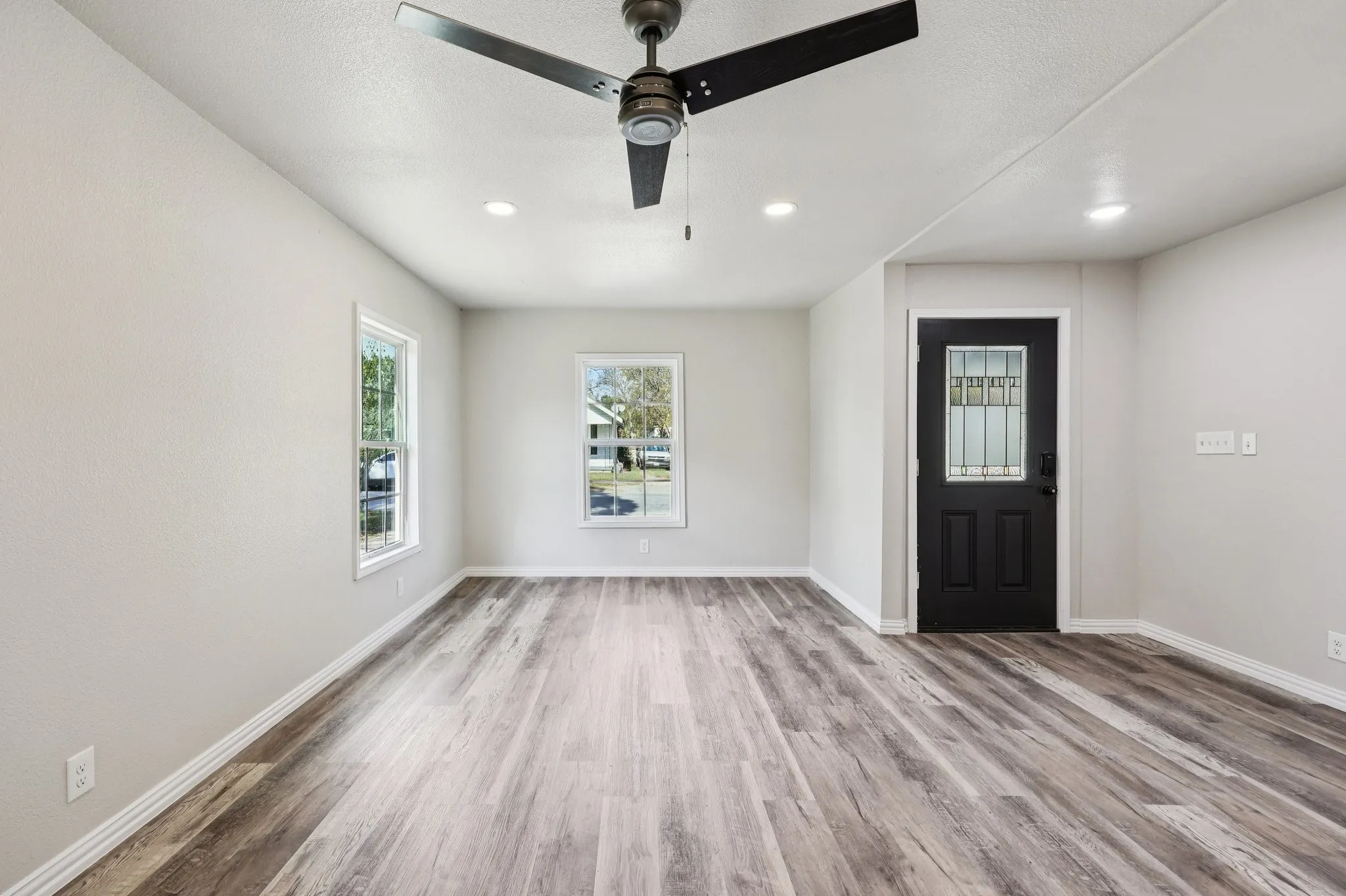 Expansive room featuring wood-finish flooring, two windows with white trim, recessed lighting, and a contemporary ceiling fan
