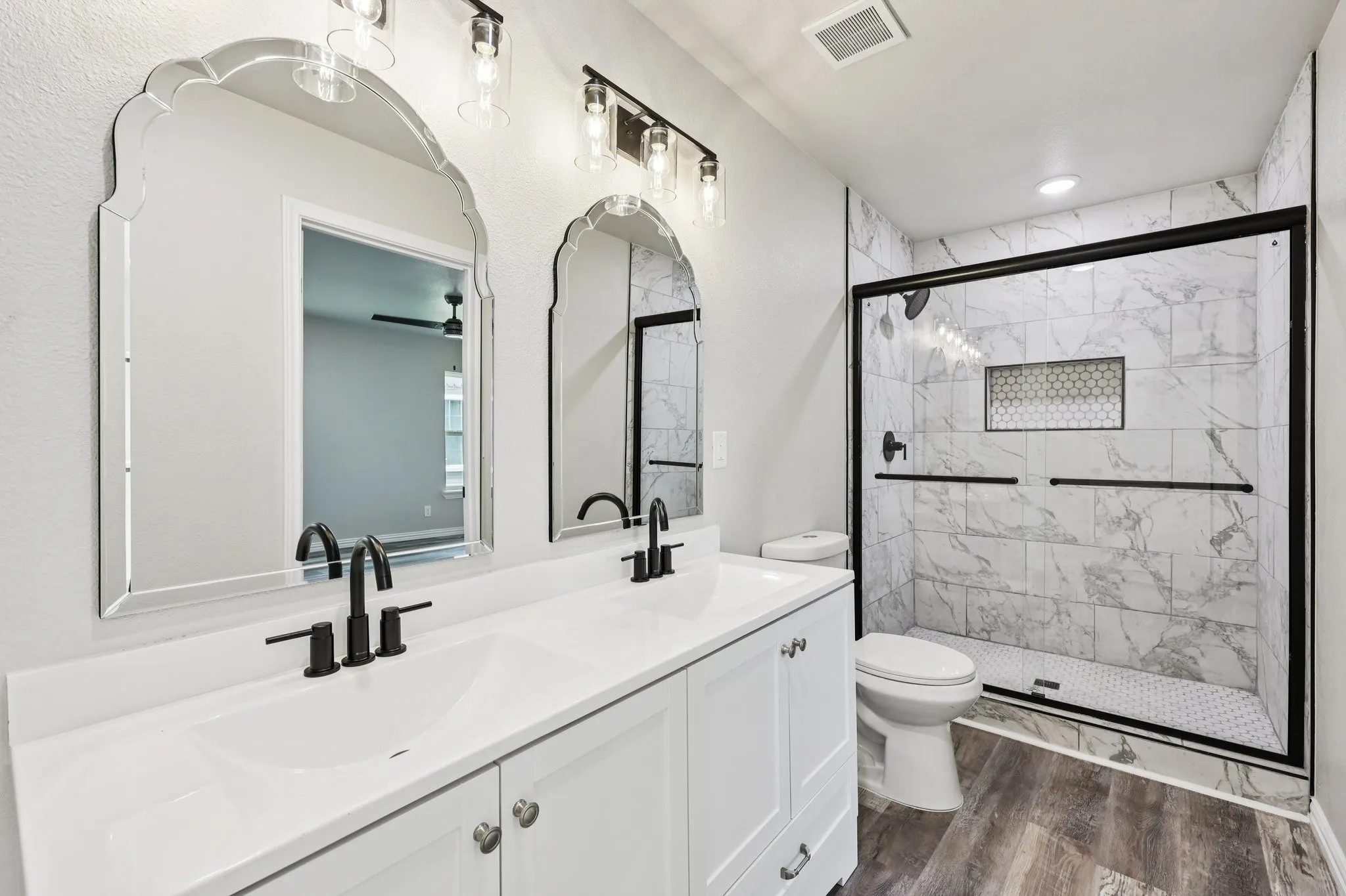 Bathroom featuring a dual vanity with white cabinetry and integrated sinks, matte black fixtures, and decorative arched mirrors