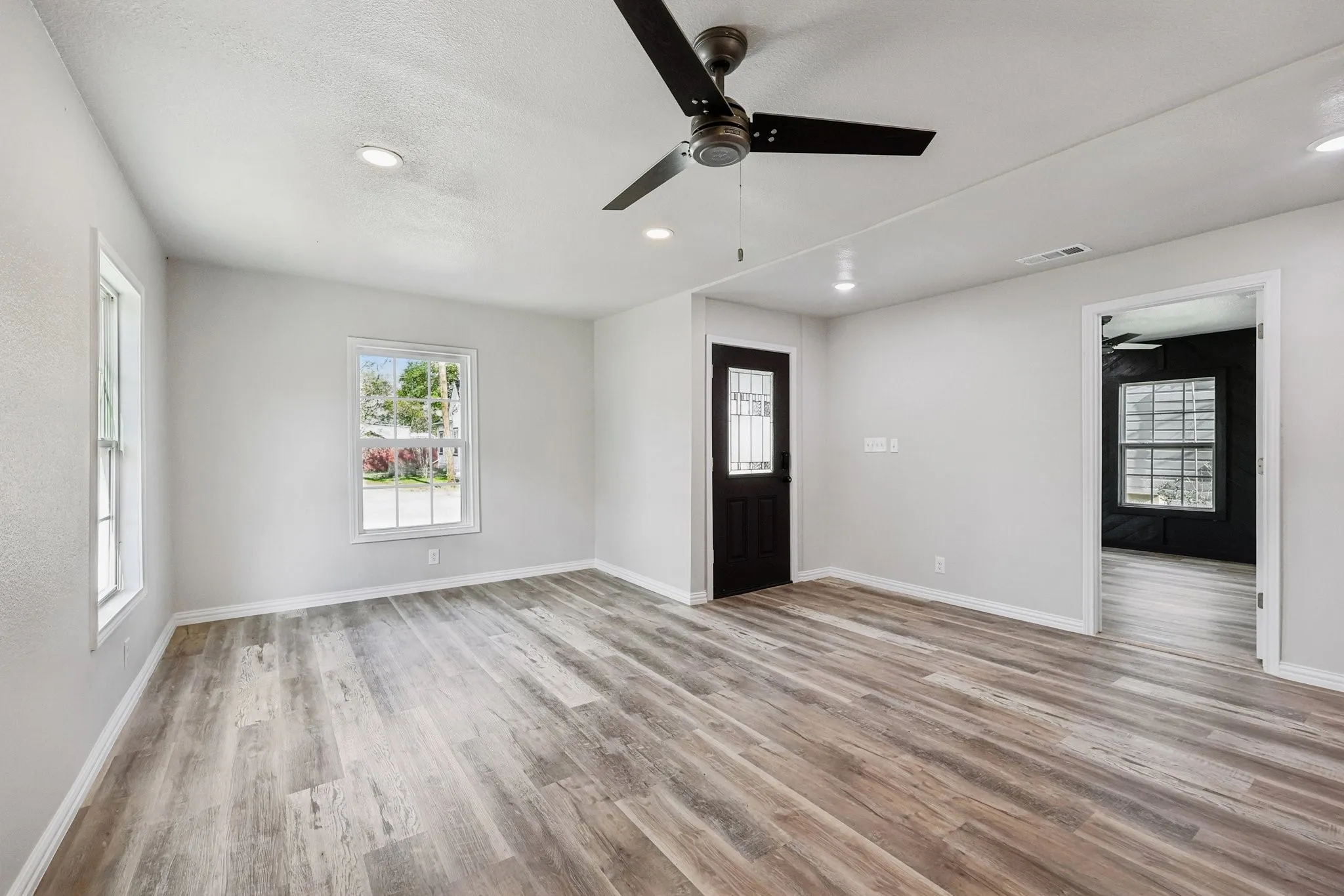 Spacious interior featuring wood-finish flooring, light grey walls, and a contemporary ceiling fan