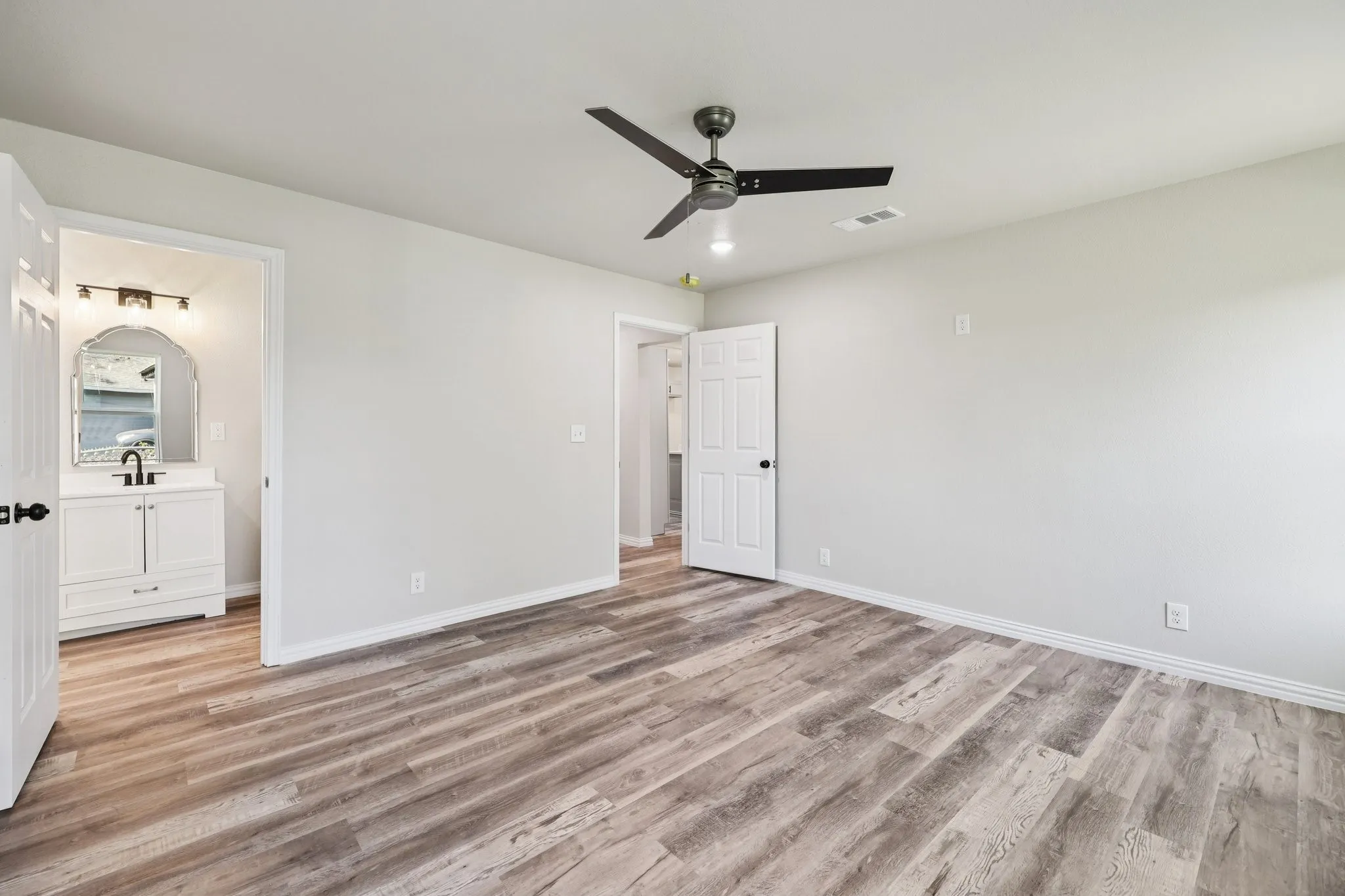 Spacious interior room featuring wood-finish flooring, light gray walls, and a ceiling fan with integrated lighting