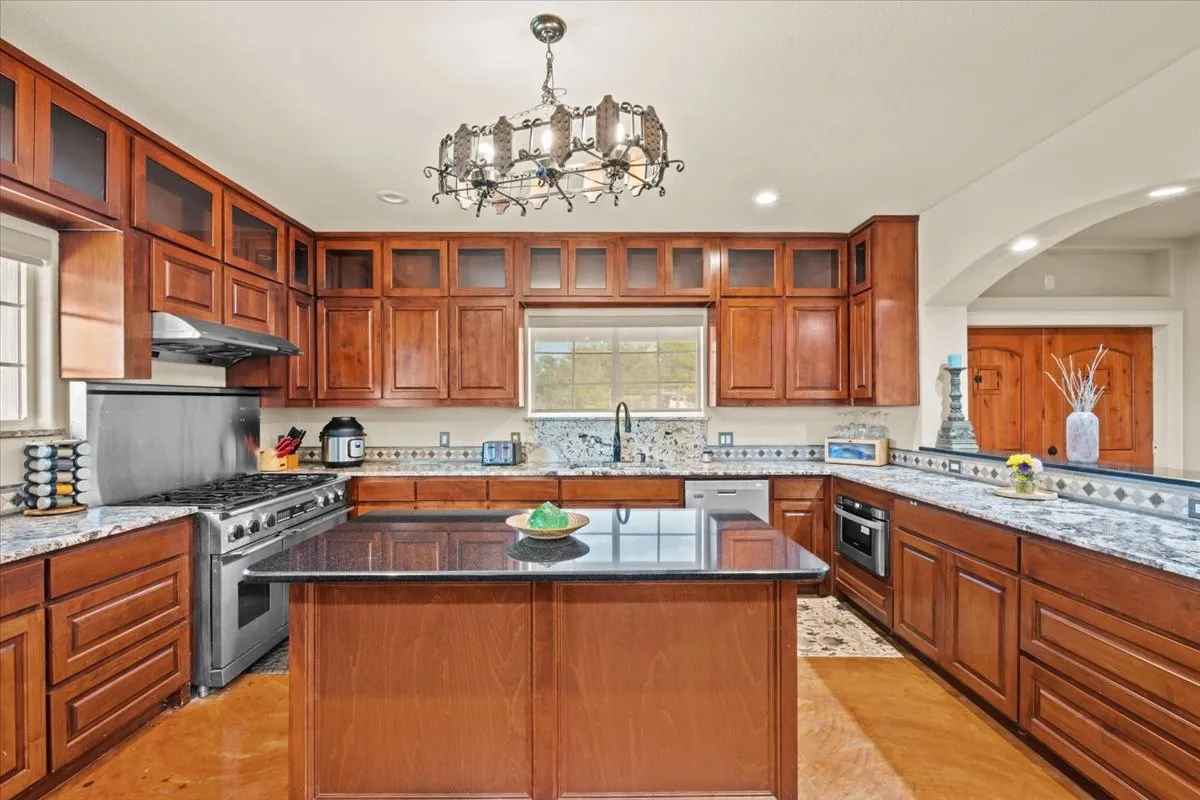 Large kitchen with stained concrete floors, island, granite counters, abundant cabinets, and commercial grade Dacor range at 3601 Oak Cir, Weatherford, TX 76088 - 3664 sq ft on 2.92 acres with a 2600 sq ft workshop