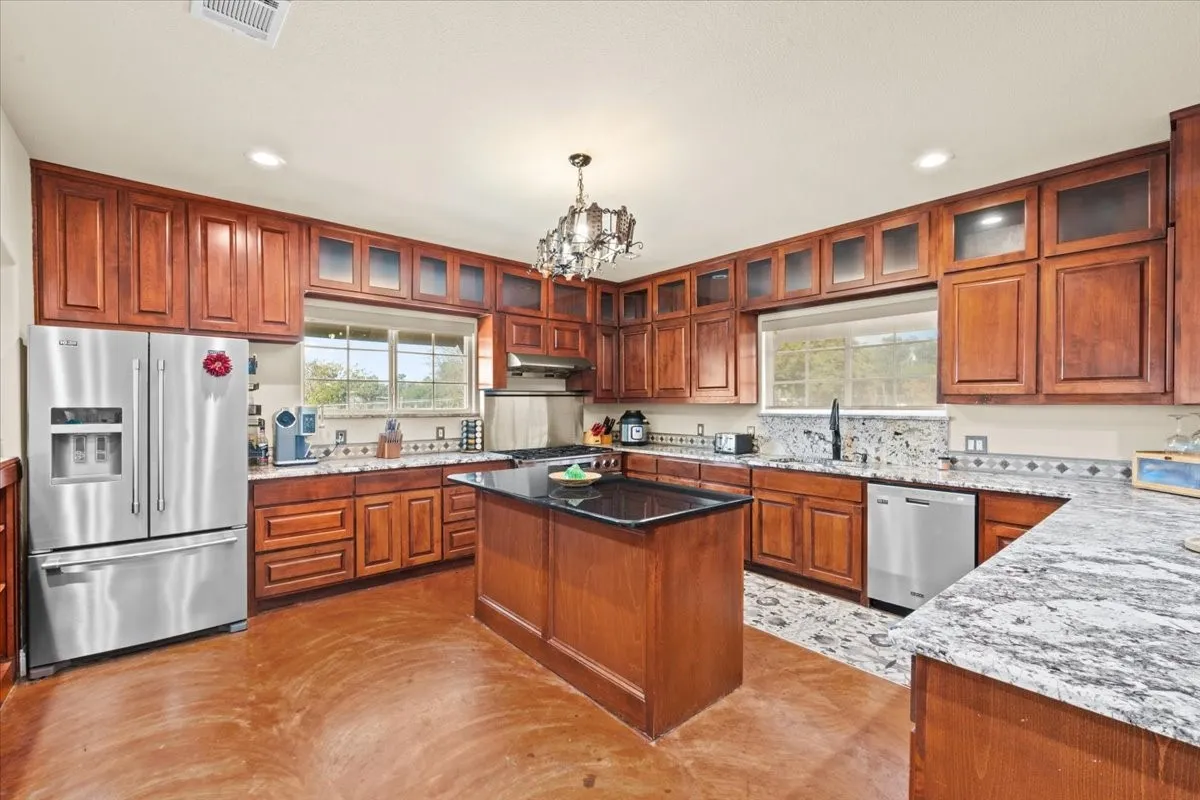Large kitchen with stained concrete floors, island, granite counters, abundant cabinets, and commercial grade Dacor range at 3601 Oak Cir, Weatherford, TX 76088 - 3664 sq ft on 2.92 acres with a 2600 sq ft workshop