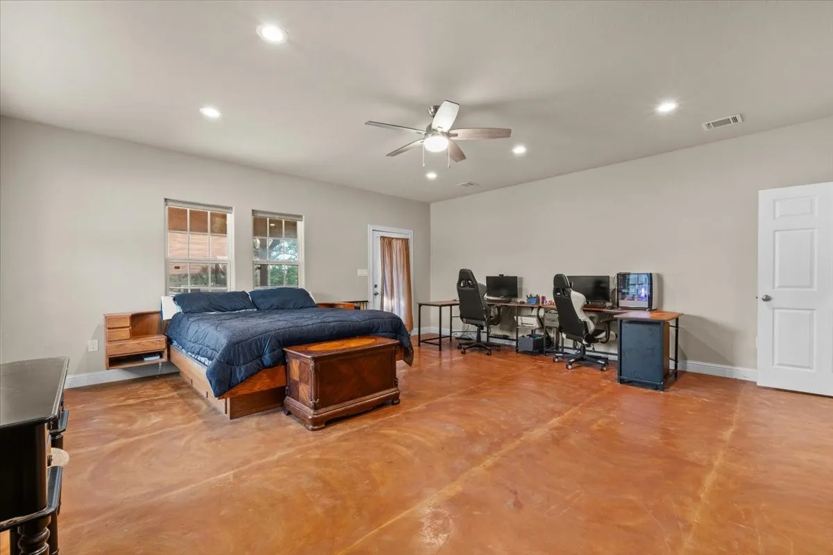 Spacious primary bedroom with stained concrete floors and door to balcony at 3601 Oak Cir, Weatherford, TX 76088 - 3664 sq ft on 2.92 acres with a 2600 sq ft workshop