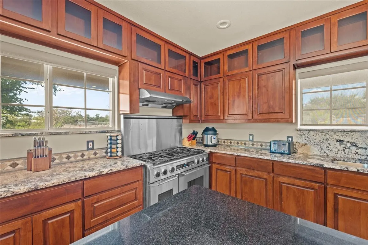 Large kitchen with stained concrete floors, island, granite counters, abundant cabinets, and commercial grade Dacor range at 3601 Oak Cir, Weatherford, TX 76088 - 3664 sq ft on 2.92 acres with a 2600 sq ft workshop