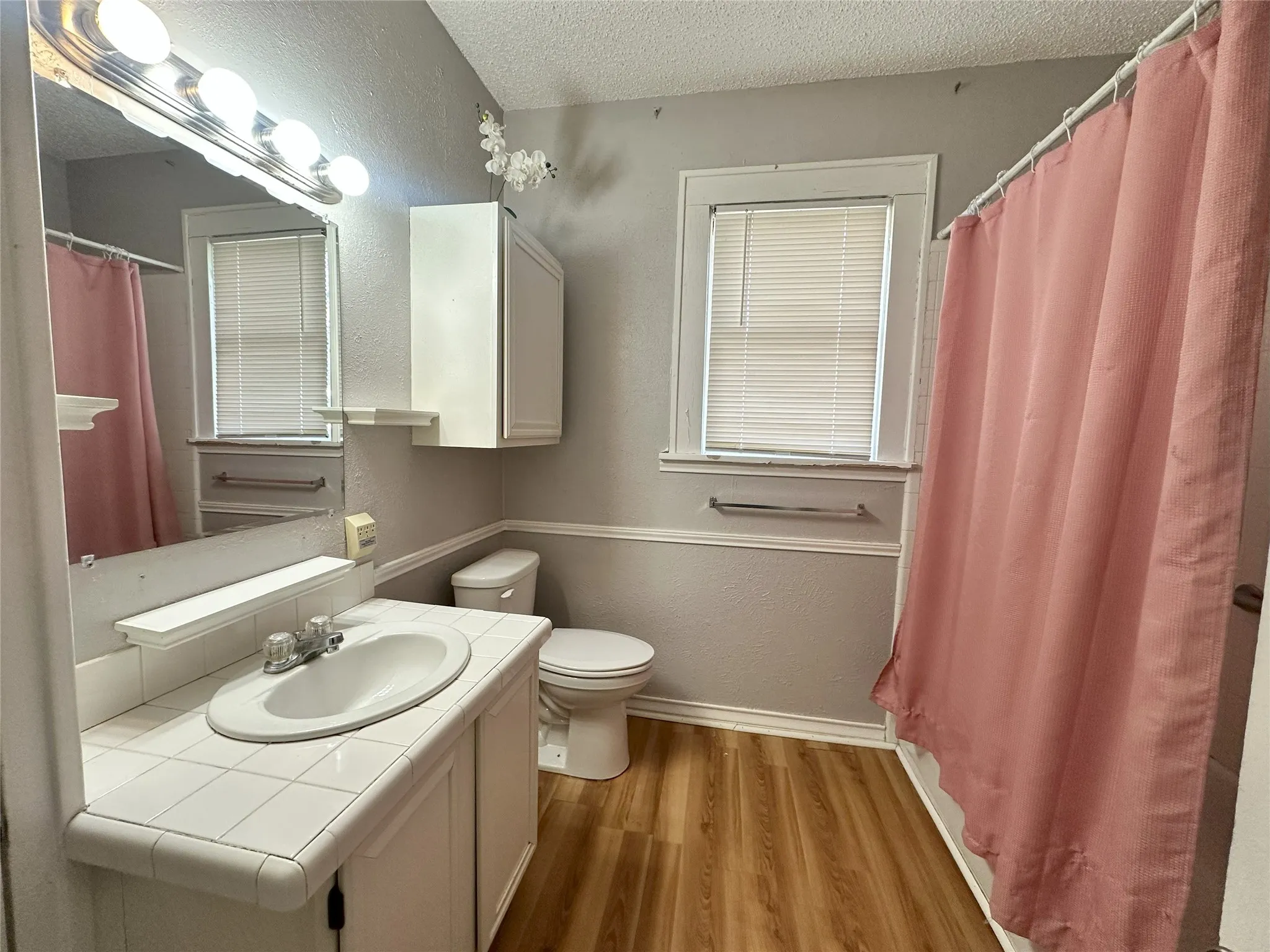 Bathroom featuring wood-finish flooring, a tiled vanity with integrated sink, and white wall-mounted cabinetry