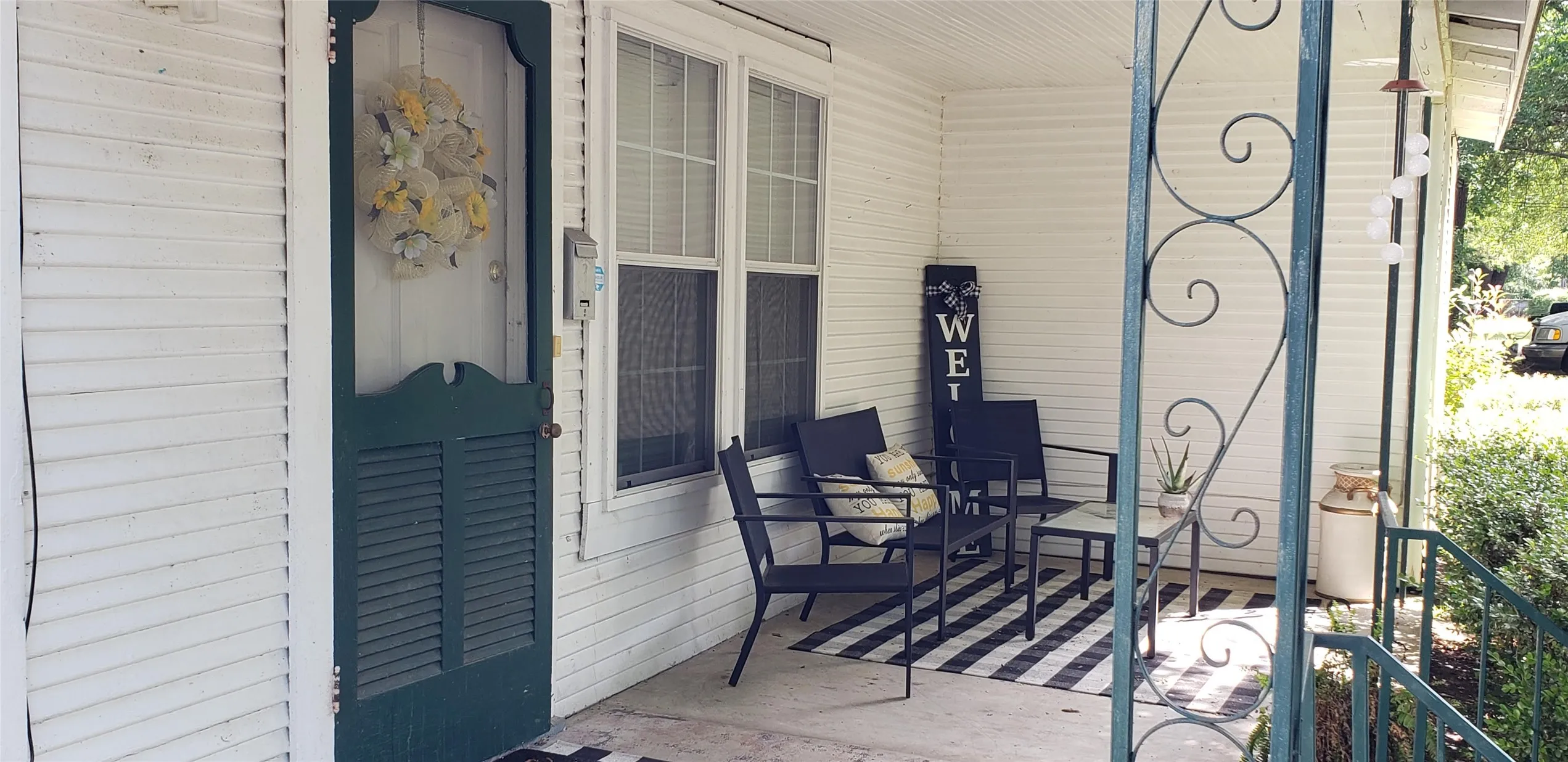 Covered front porch with white siding, a dark green screen door, and vertical windows