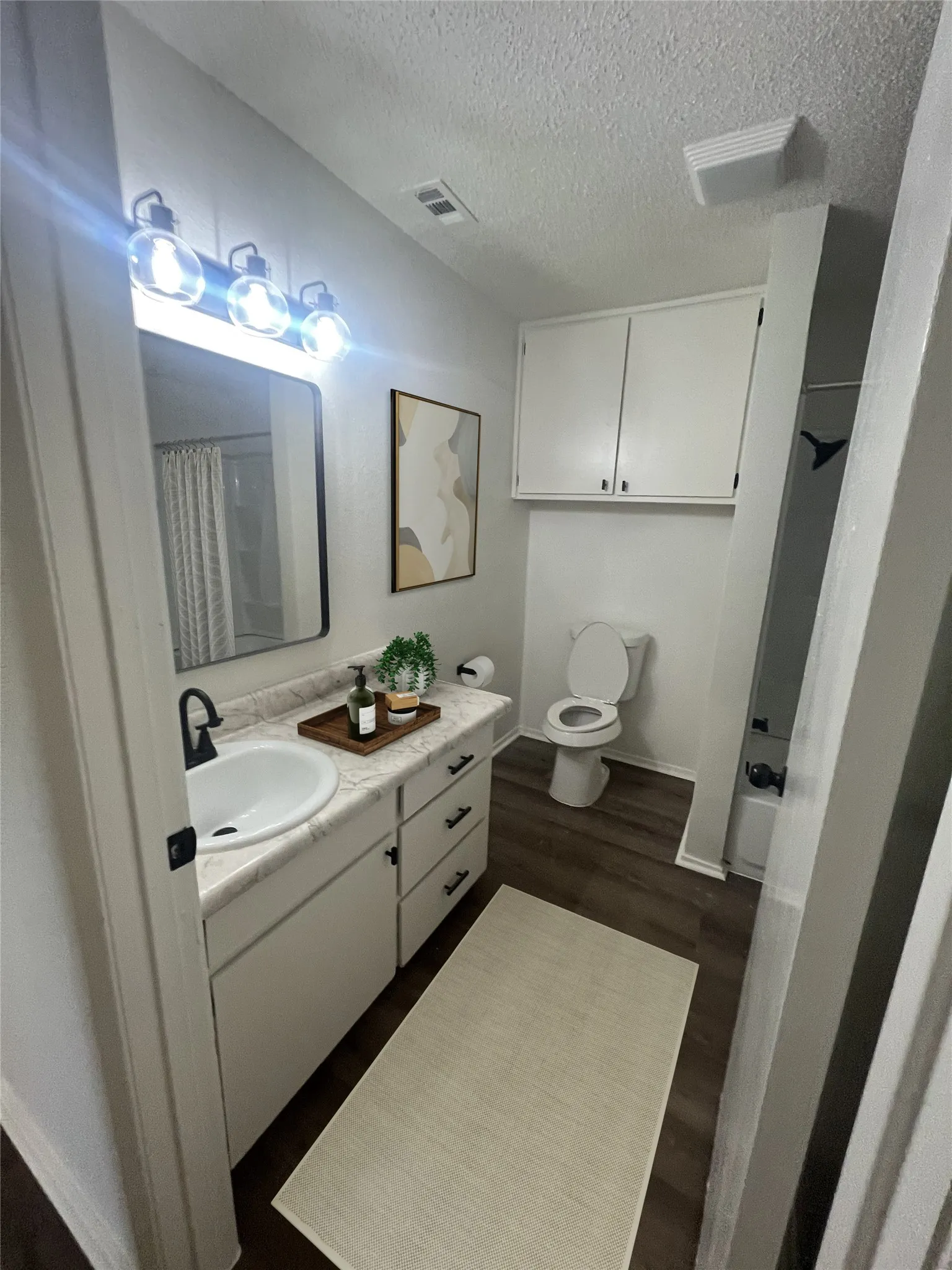 Full bath featuring a textured ceiling, vanity, wood finished floors, and a shower with shower curtain