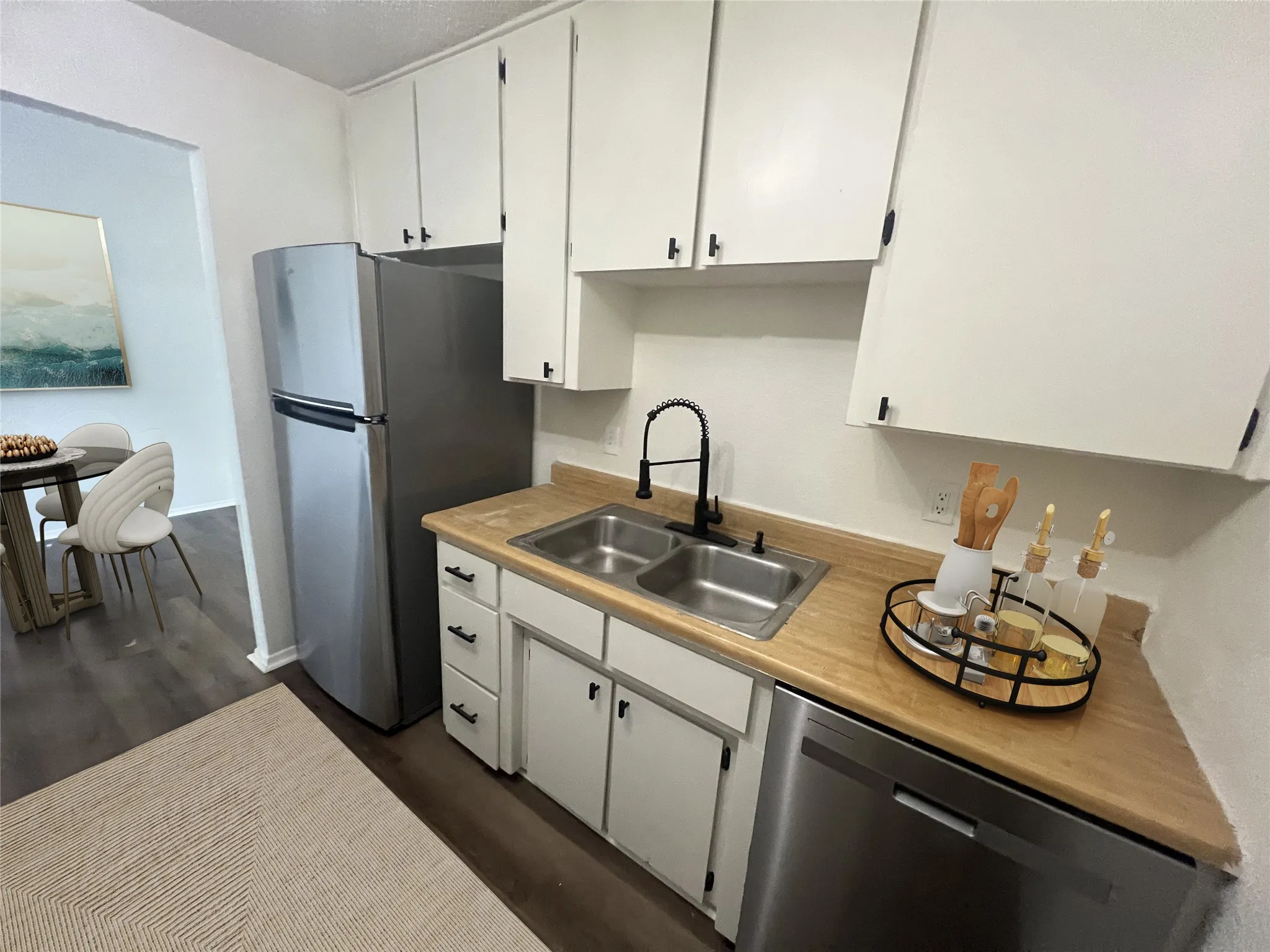 Kitchen with stainless steel appliances, light countertops, dark wood-type flooring, and white cabinetry