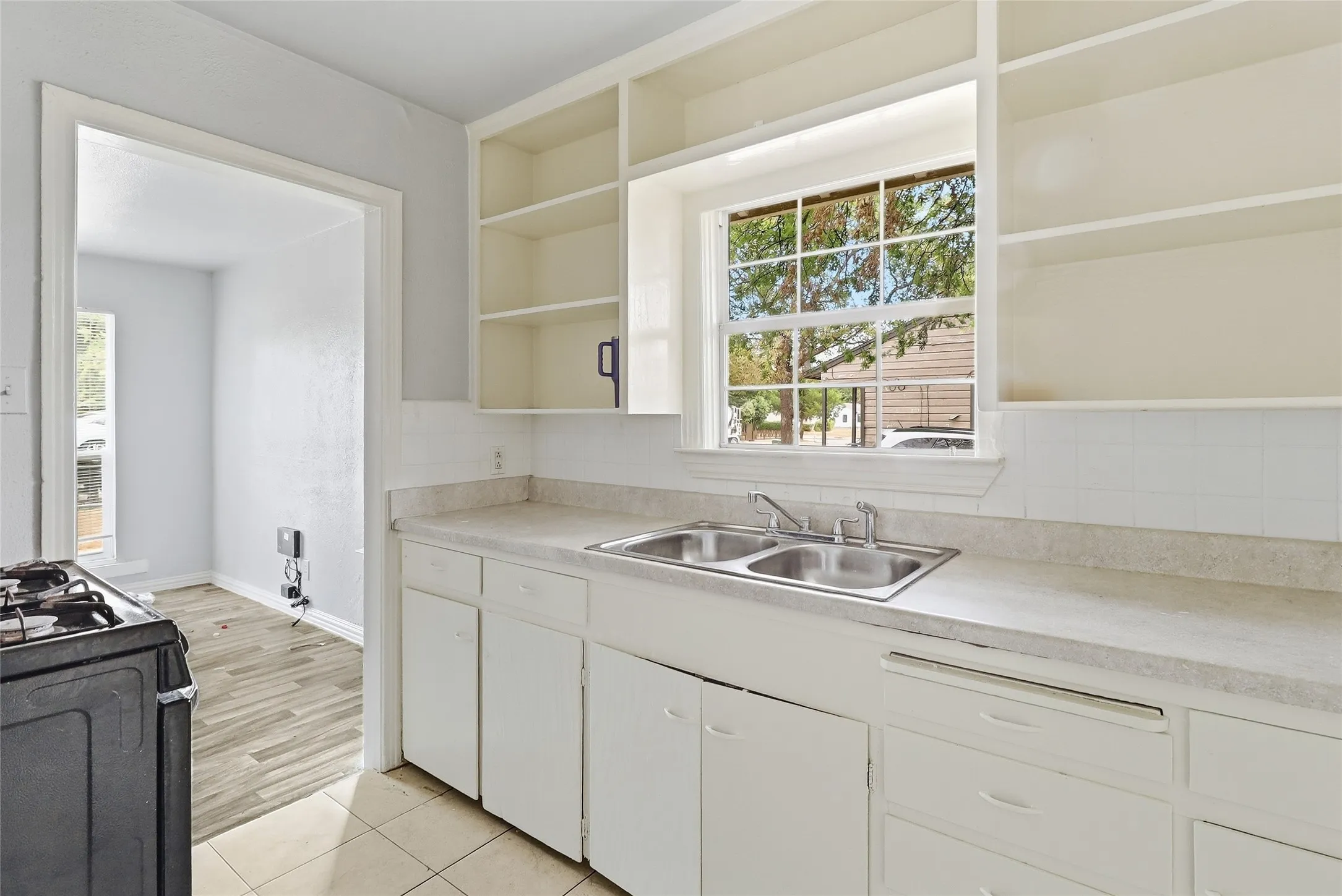 Kitchen featuring white cabinetry, a dual-basin stainless steel sink, light-toned countertops, and a window with exterior views