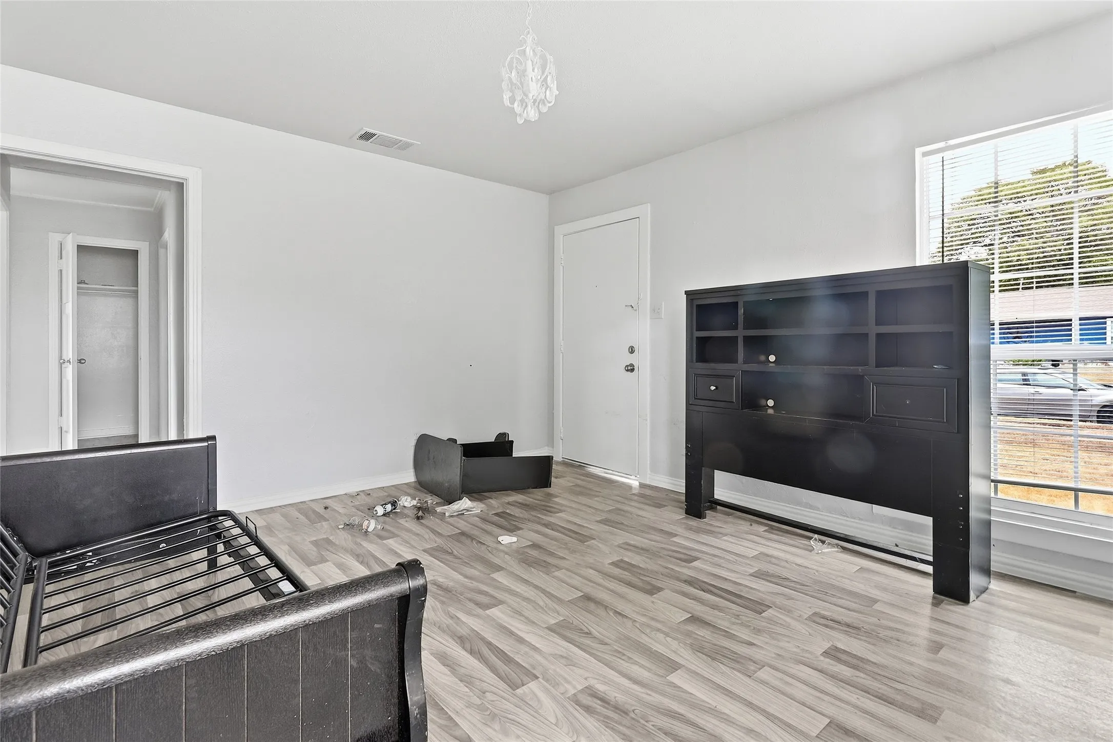 Light-colored wood-finish flooring, white painted walls, and a window with horizontal blinds