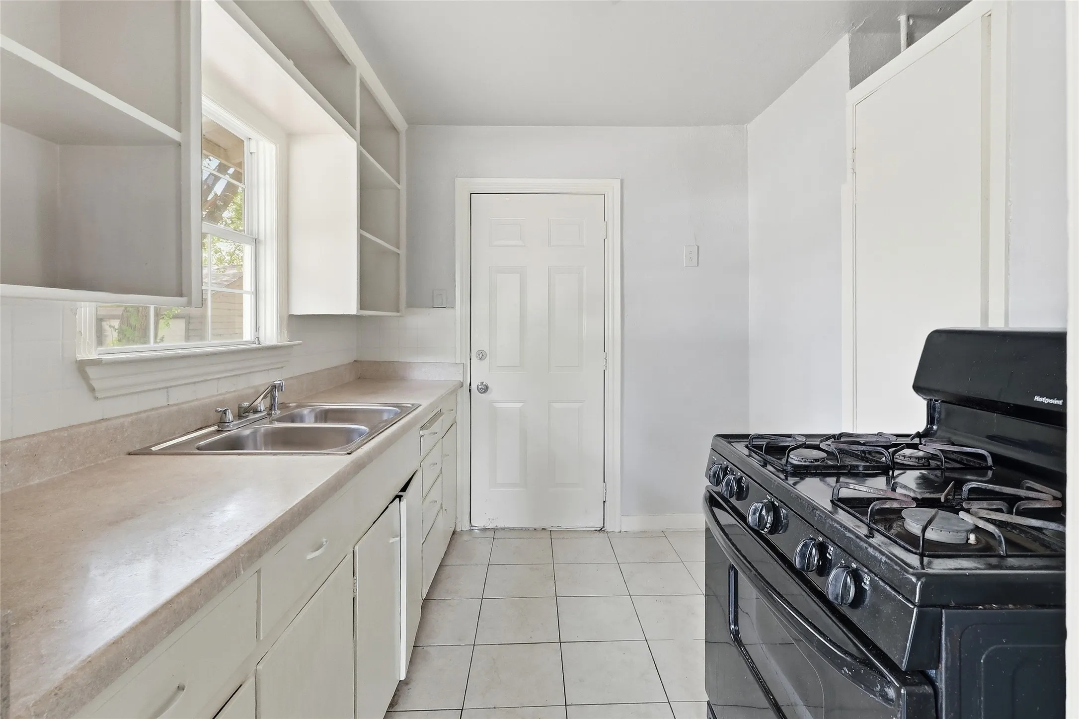 Kitchen featuring a gas range, dual basin sink, white cabinetry, and light-toned tile flooring