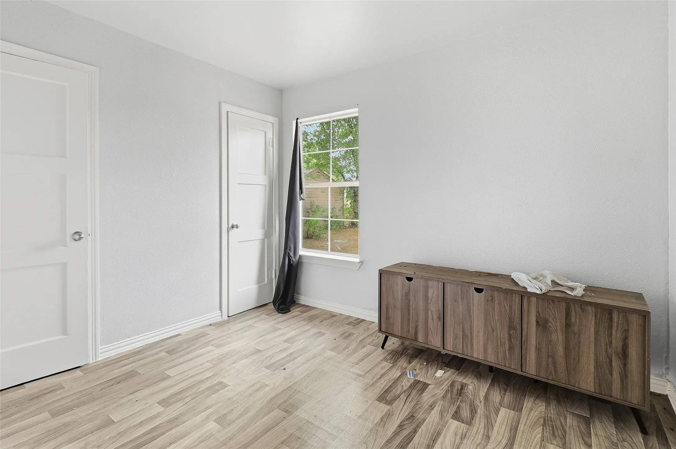 Bright room featuring wood-finish flooring, white walls, and a window