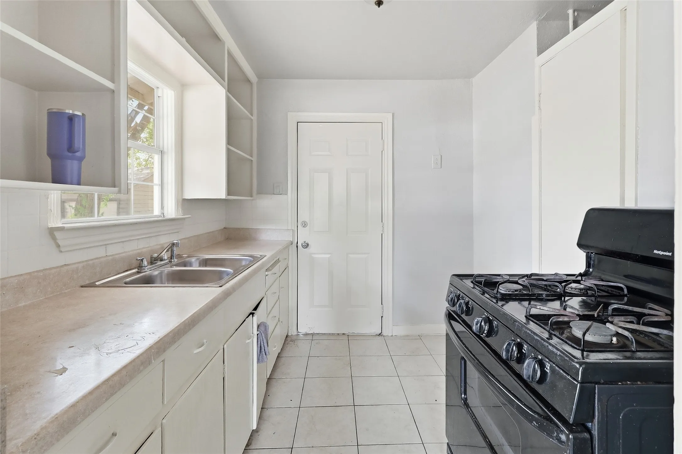Kitchen featuring a dual basin sink, white cabinetry, a window with trim, and tile flooring