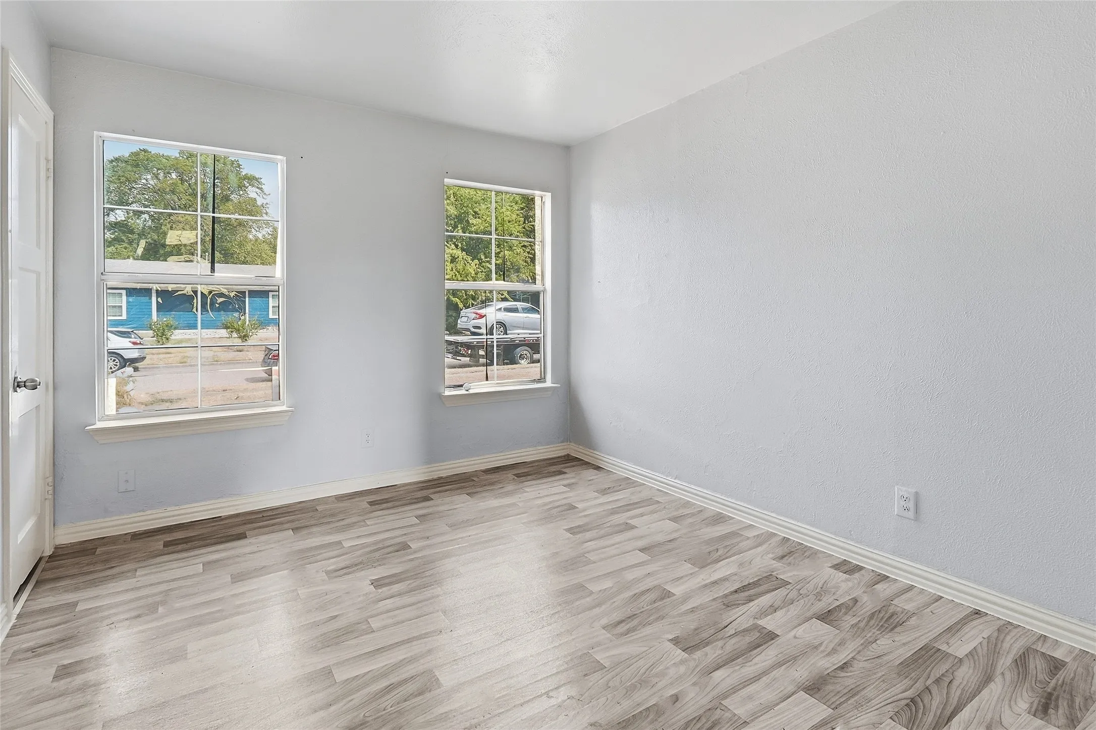 Light-filled room featuring two windows, wood-finish flooring, and a white interior door