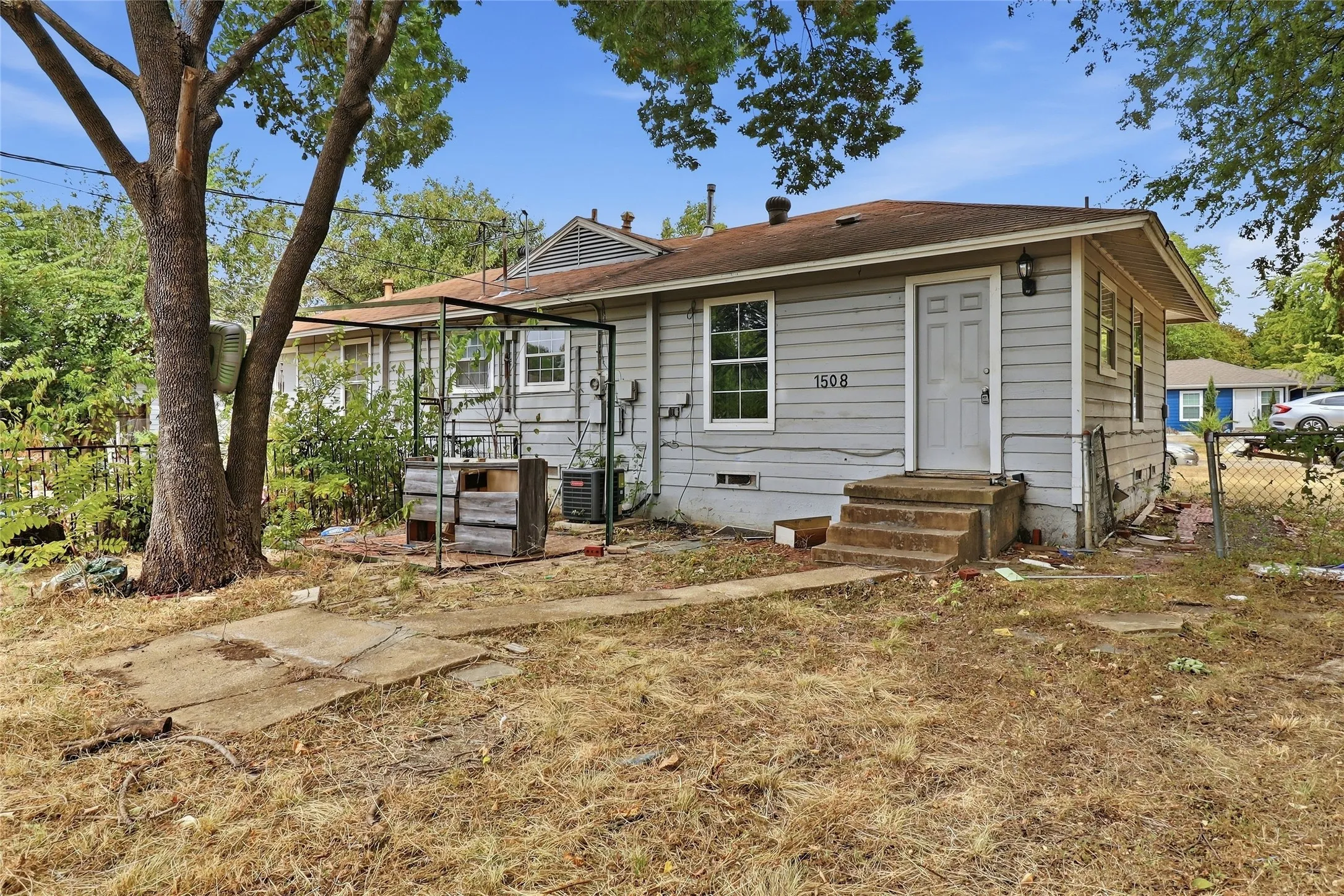 Single-story residence featuring horizontal siding exterior, covered front porch with wooden steps, and mature shade trees on the property