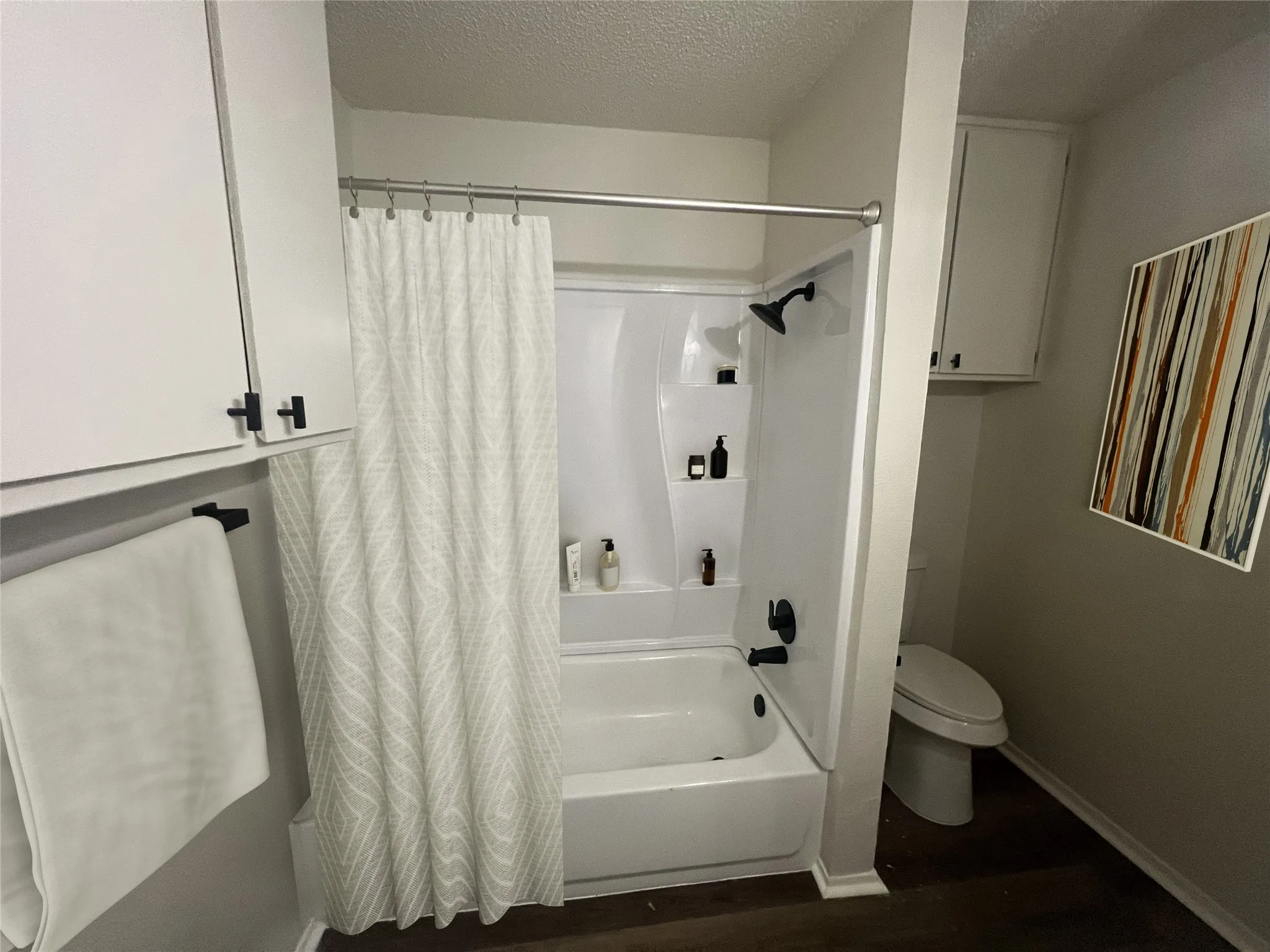 Bathroom featuring a textured ceiling, shower / bath combination with curtain, and wood finished floors