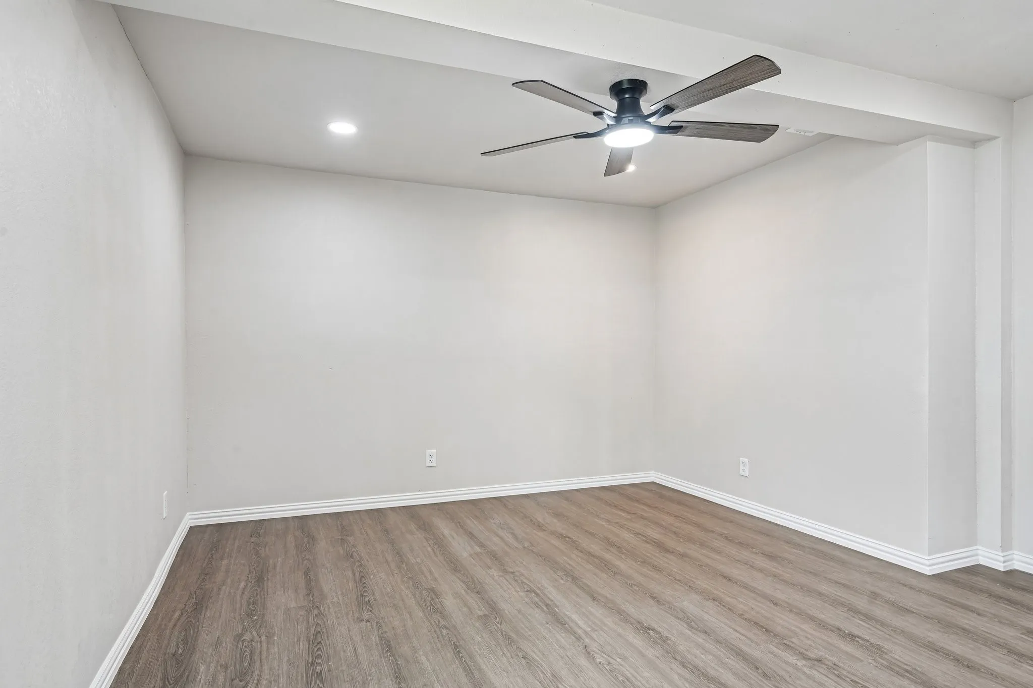Spacious room featuring wood-finish flooring, light gray walls, white baseboards, and a modern ceiling fan with integrated lighting