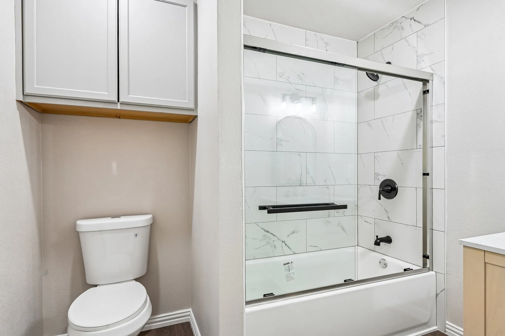 Tub and shower combination featuring white marble-look subway tile and dark bronze fixtures