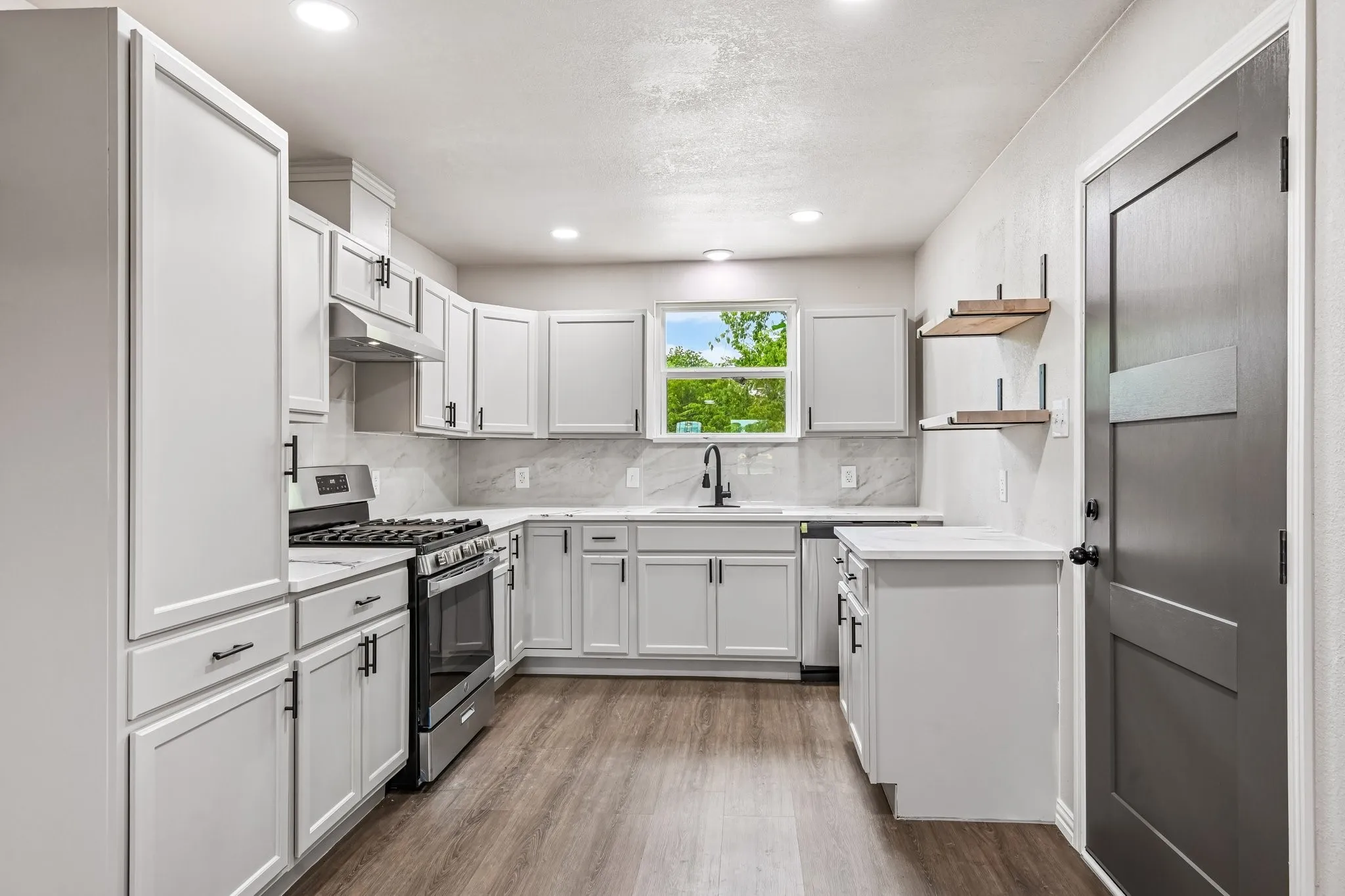 Modern kitchen featuring light gray cabinetry, stainless steel appliances, a matte black faucet, wood-finish flooring, and open shelving