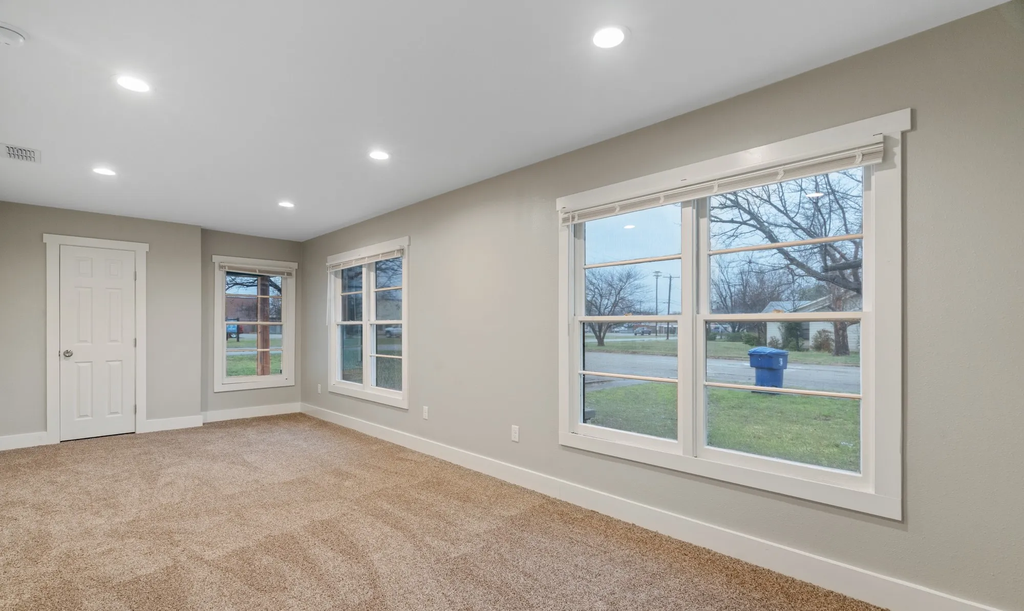 Recessed lighting, light-colored walls, white trim, white paneled door, and multiple windows