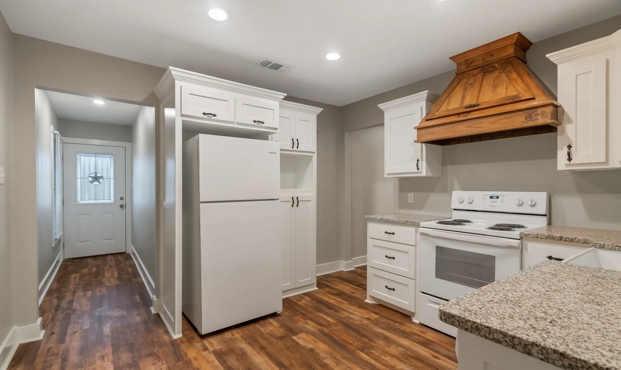 Wood-finish flooring, white cabinetry with dark hardware, built-in range, wood range hood, and light-colored countertops