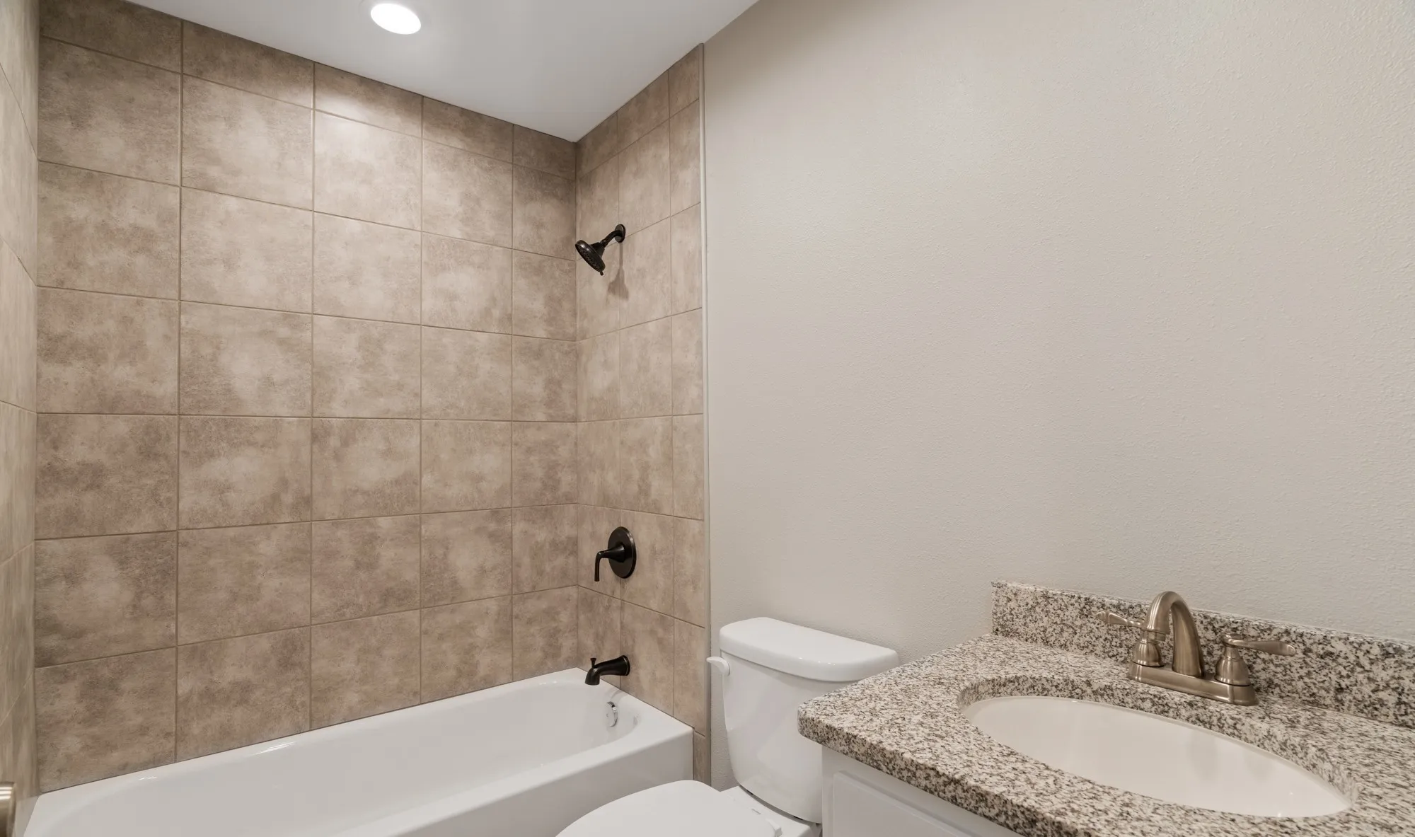 Full bathtub with tiled surround, a toilet, and a vanity with a stone countertop and undermount sink