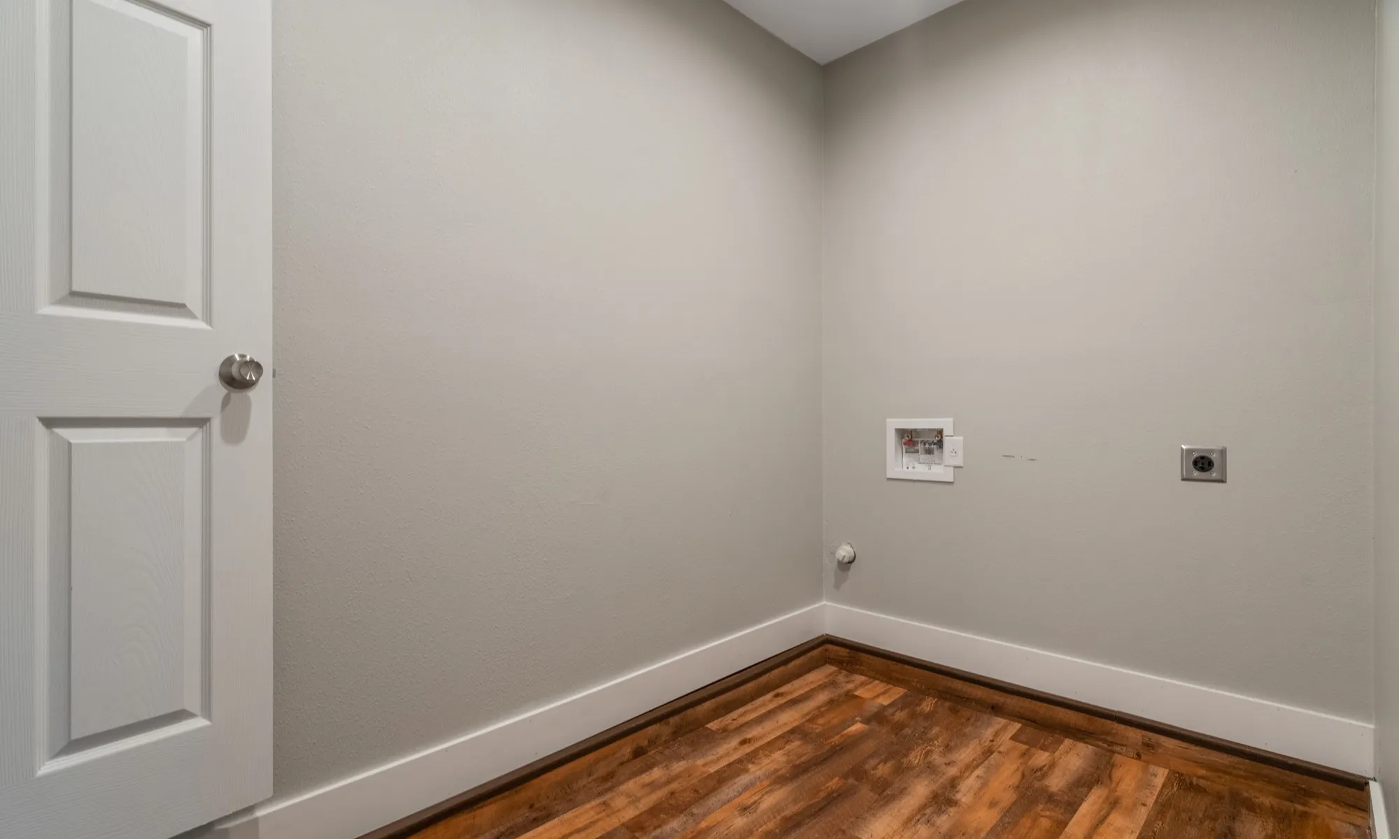 Wood-finish flooring with crisp white baseboards, a paneled door with brushed nickel hardware, and neutral wall tones
