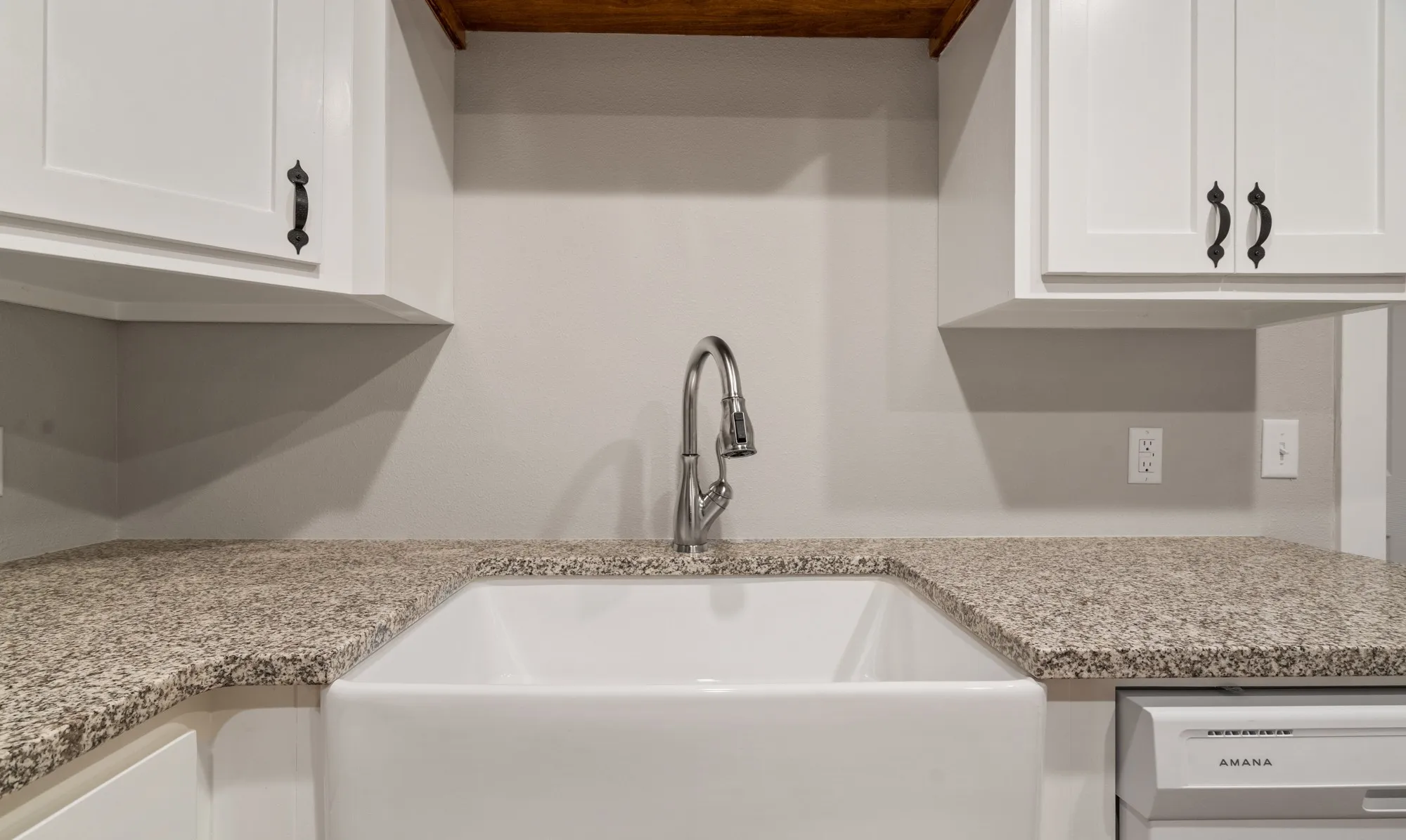 White farmhouse sink with a gooseneck faucet, light-toned speckled countertops, and white upper cabinetry with dark hardware