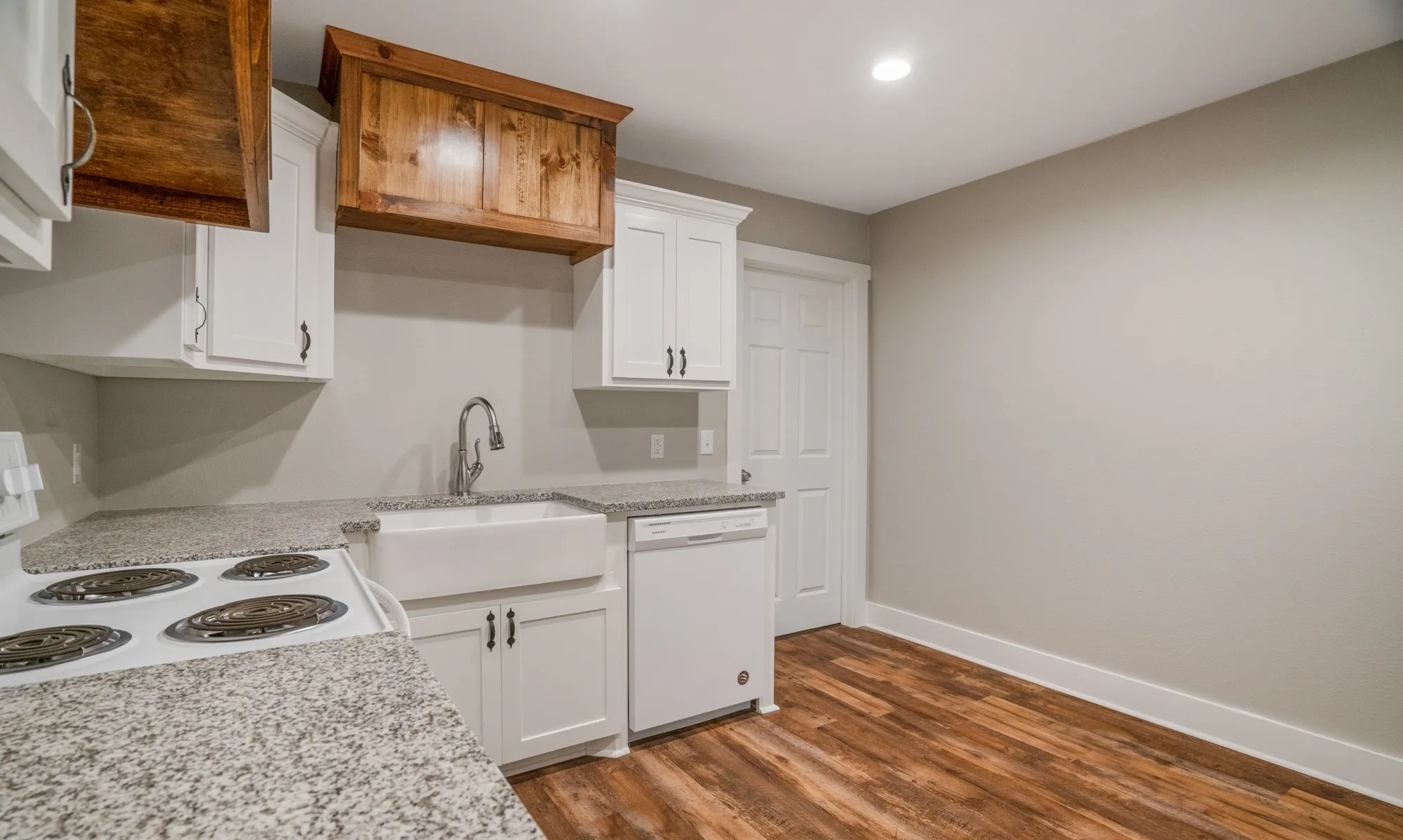 White cabinetry, wood-finish flooring, granite-style countertops, farmhouse sink, and stainless-steel faucet