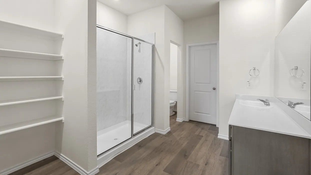 Walk-in shower with clear glass enclosure, double vanity with dual sinks, white countertop, wood-finish flooring, and built-in shelving