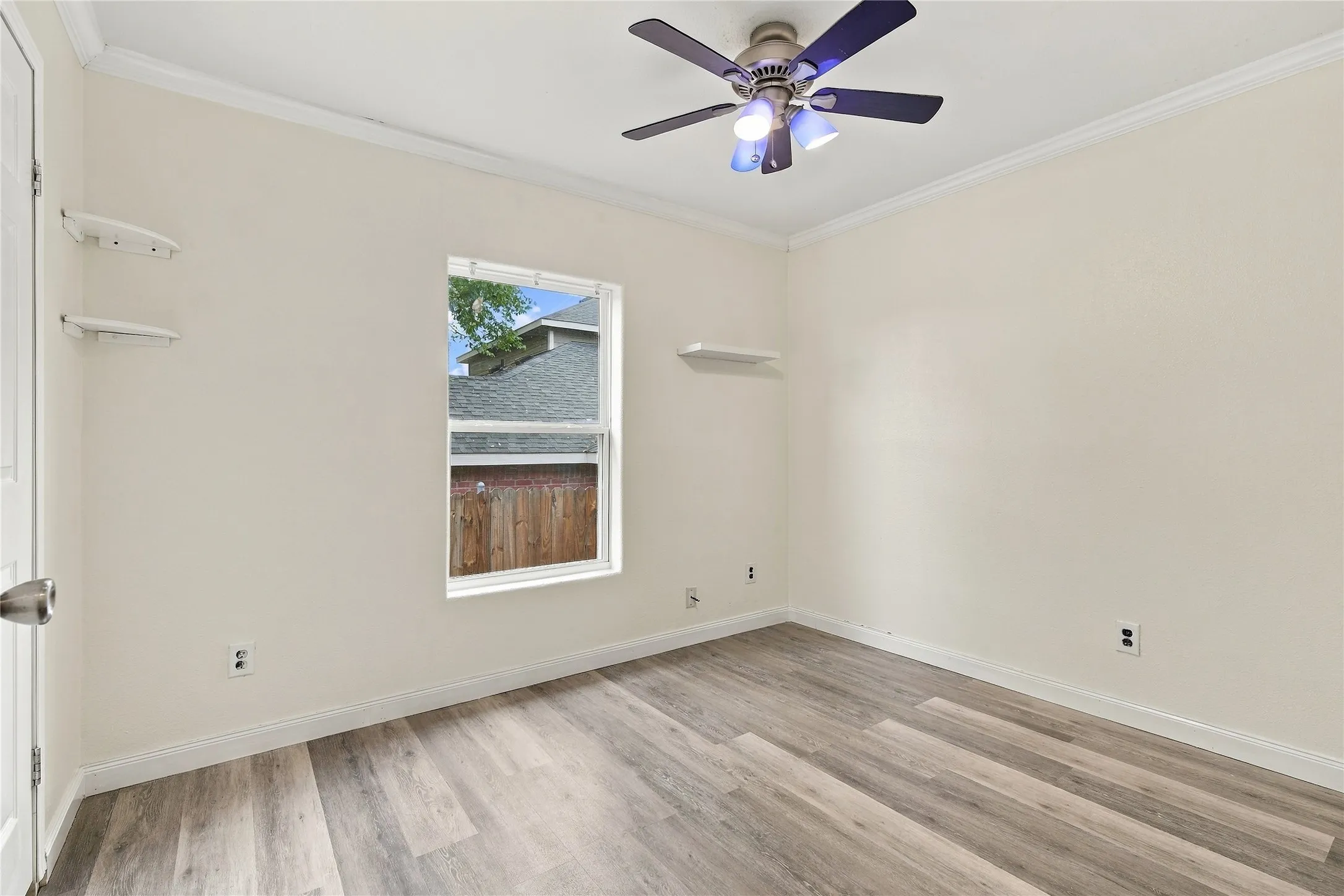 Light-toned walls, wood-look flooring, white window trim, ceiling fan with integrated lighting, and white crown molding