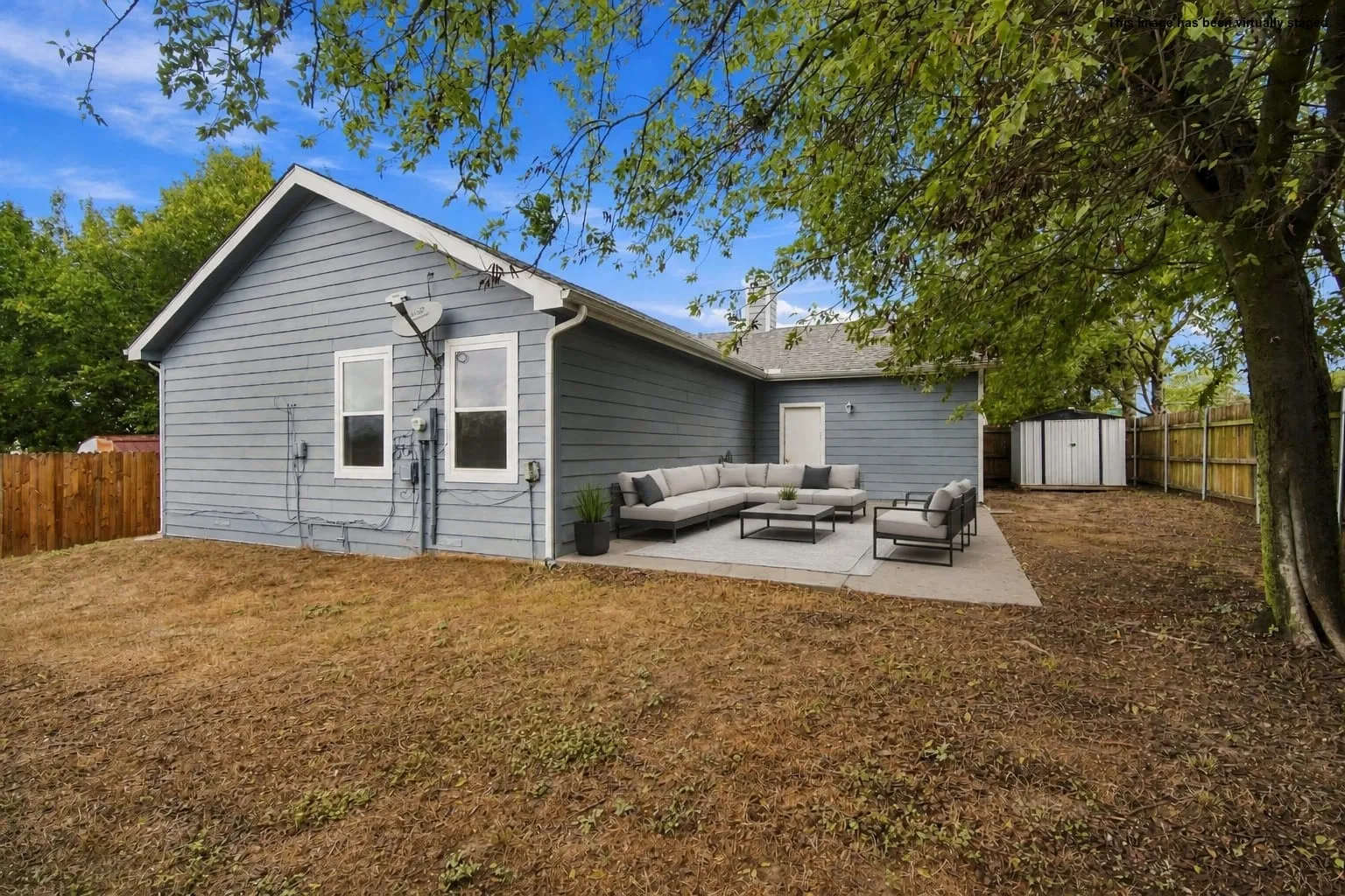 Virtually Staged Expansive backyard with a concrete patio, wood fencing, and a storage shed