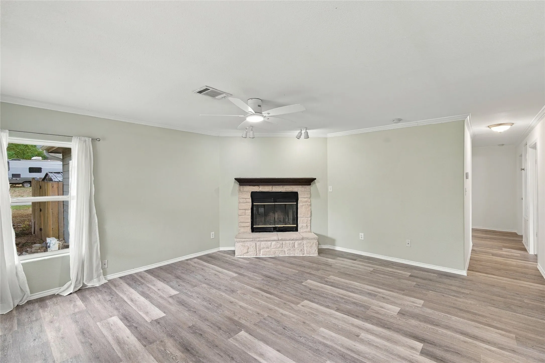 Spacious living area showcasing wood-look flooring, a fireplace with decorative surround, ceiling fan, and abundant natural light