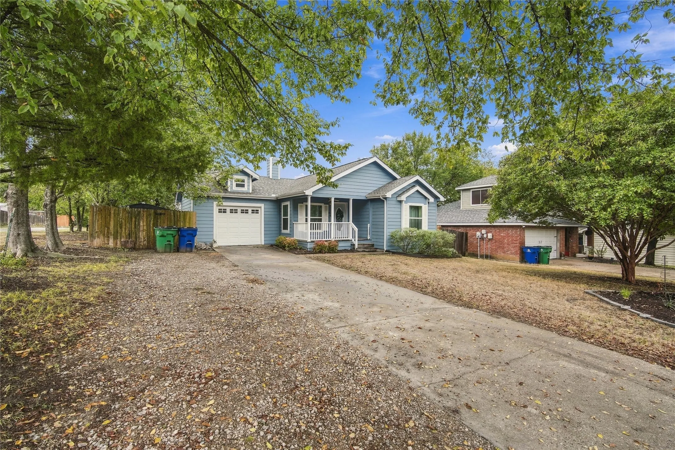 Light blue exterior siding, white trim, covered front porch with white railings, attached garage, and extended gravel driveway
