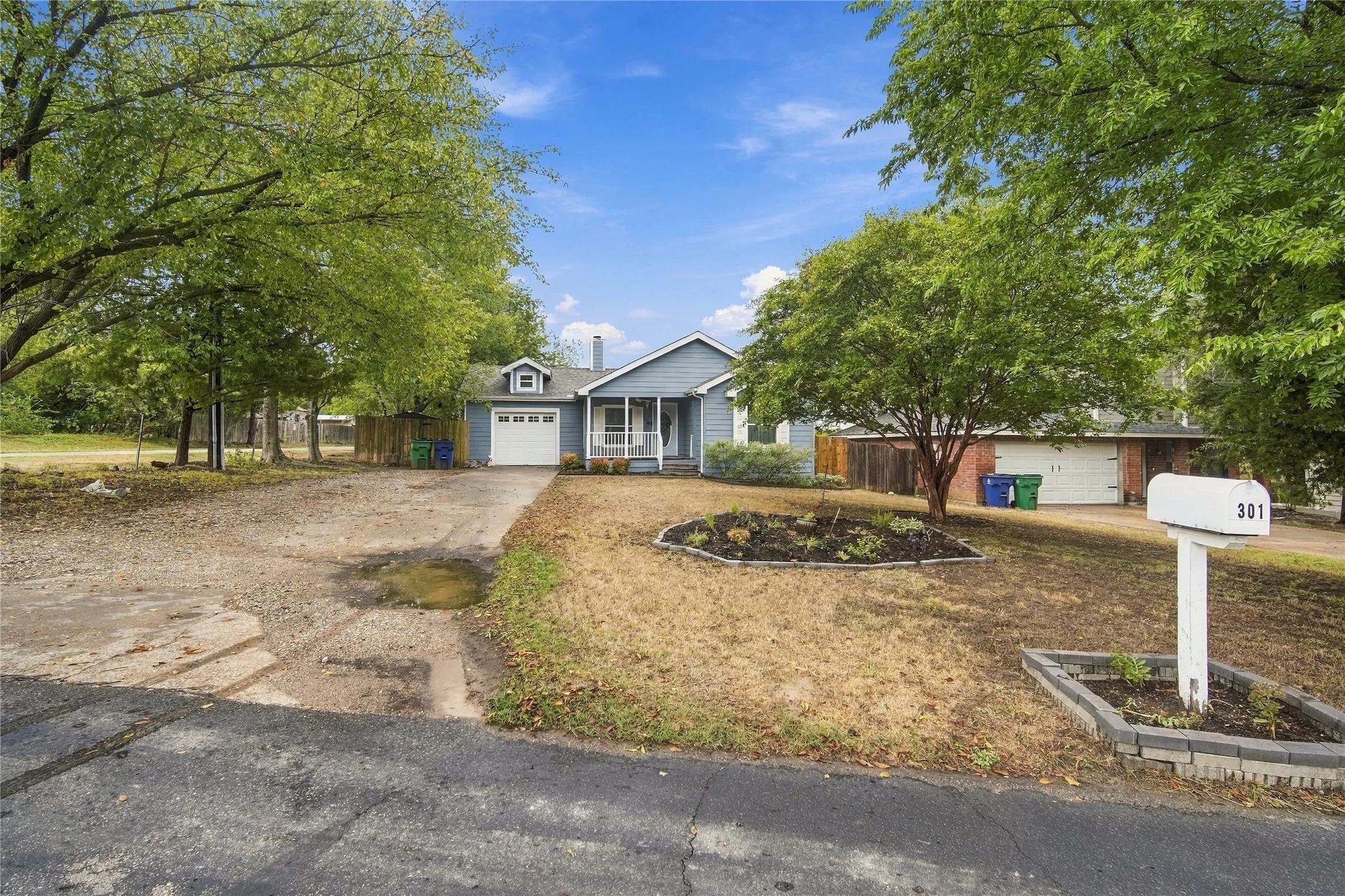 Light blue siding exterior with white trim, covered front porch, attached single-car garage, and established front yard landscaping