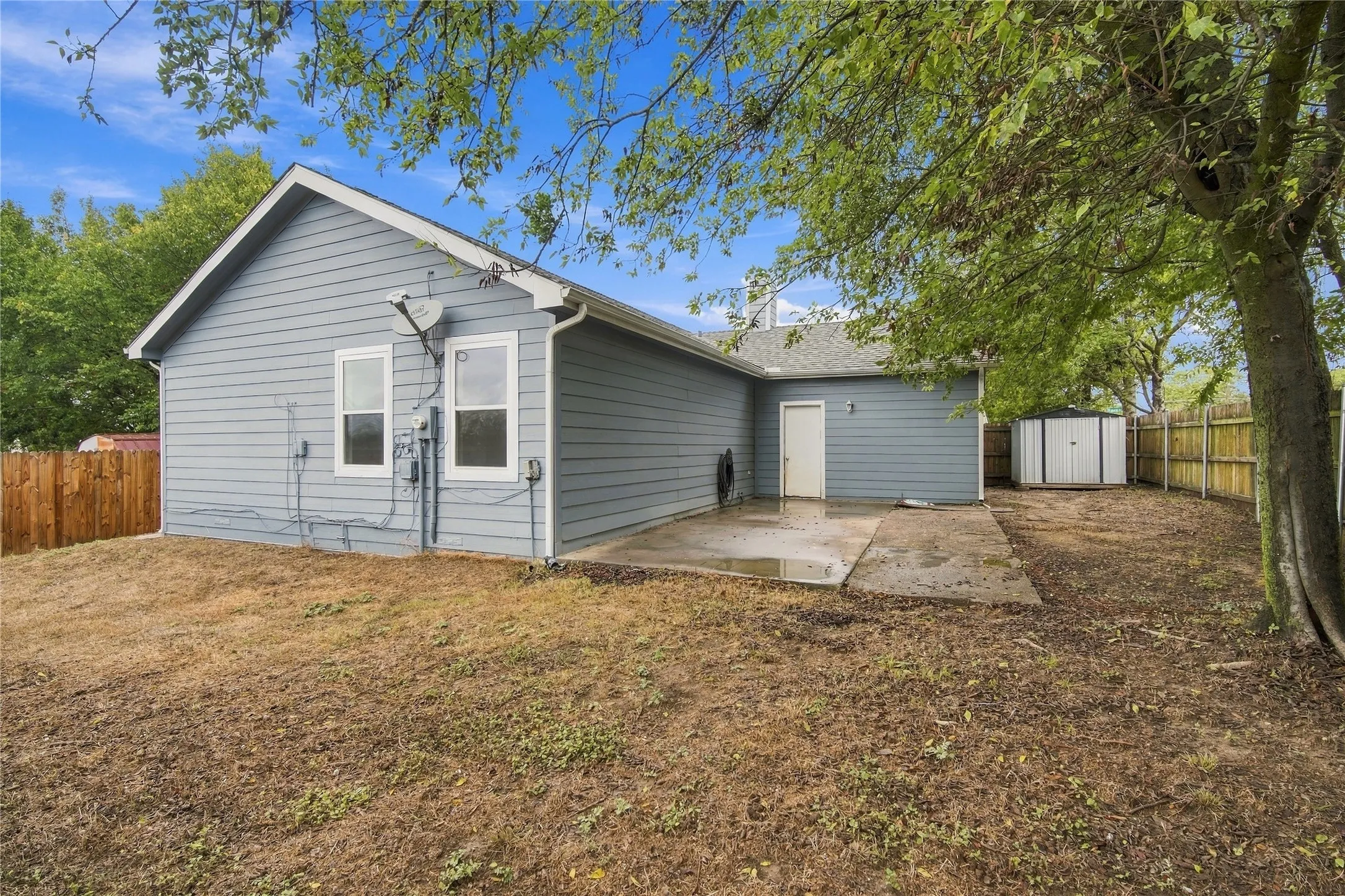 Blue siding exterior with white trim windows, concrete patio, a utility door, and a storage shed