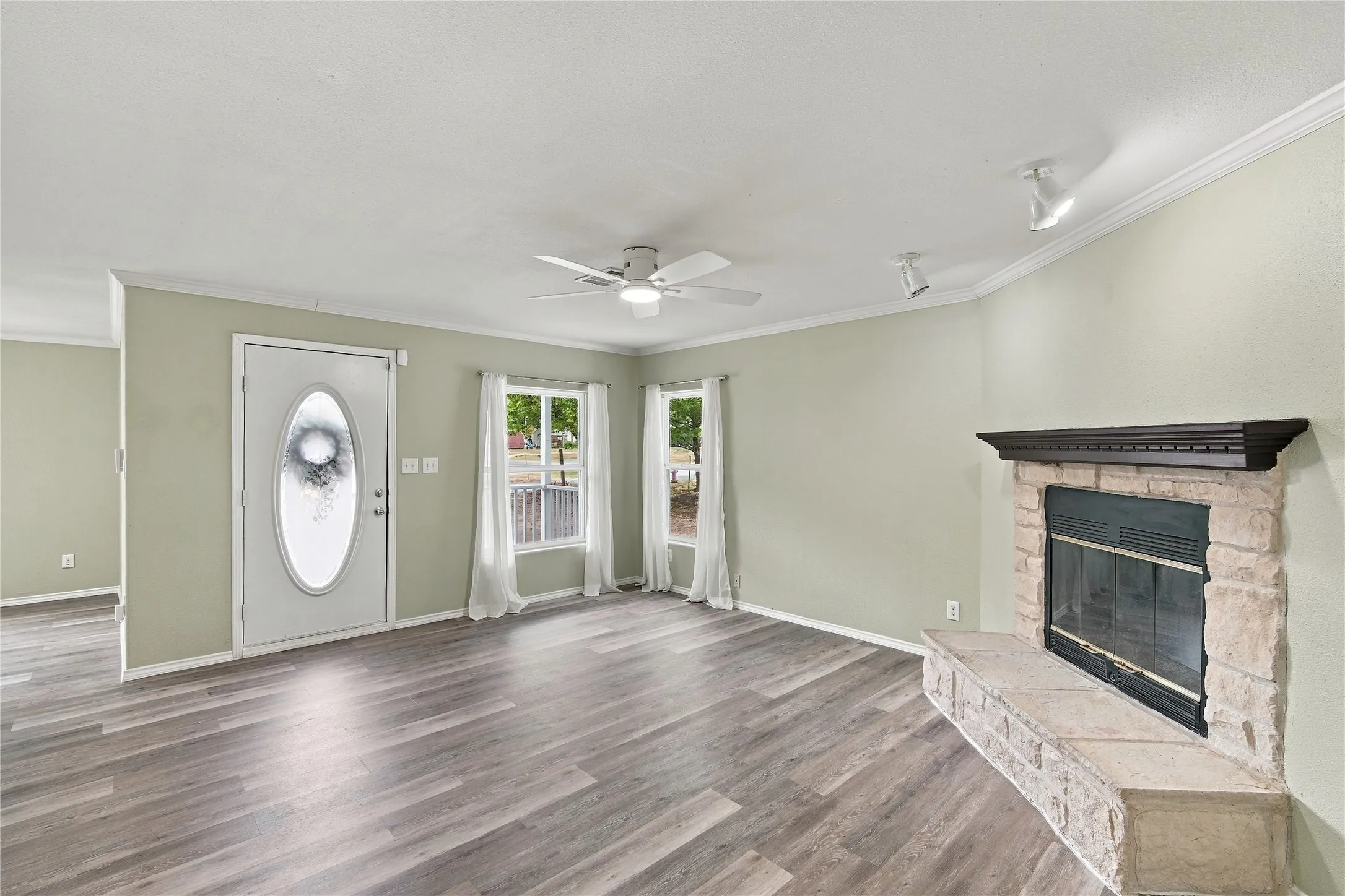 Living space featuring wood-look flooring, a stone-surround fireplace with a dark wood mantel, multiple windows, and a ceiling fan